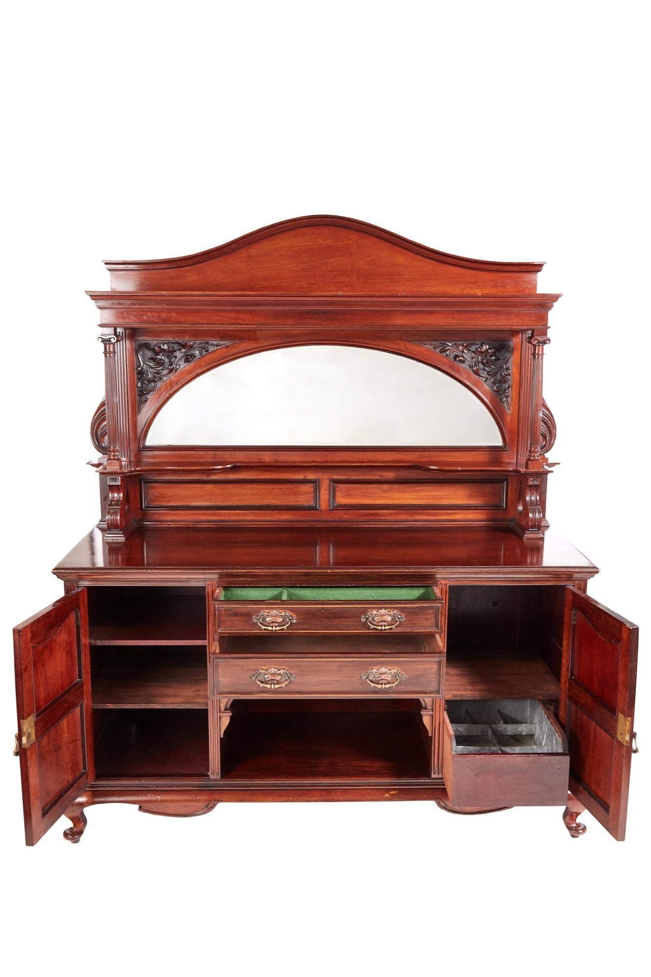 This is a large quality antique carved mahogany sideboard by Maple & Co. It boasts an attractive arched mirrored back with projecting flanking fluted columns. The striking base has two central drawers and recessed shelf below flanked by a pair of