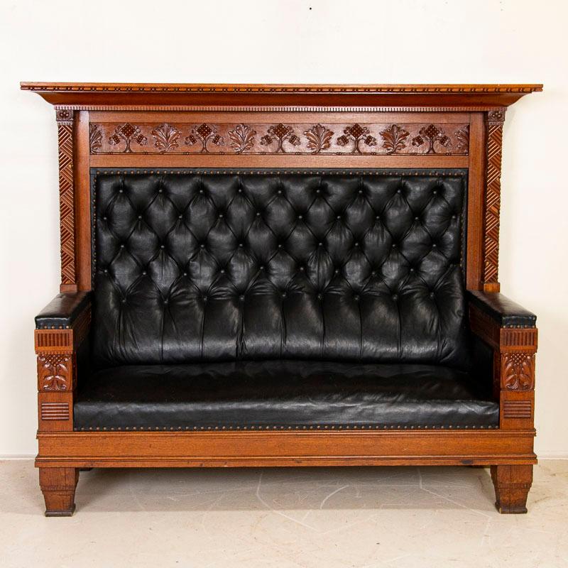 This impressive tall bench is accented with carved details along sides, arms and back. The high back is made more dramatic with tufted black leather continuing up from the seat and arm rests. Minor expected age related wear (small scratches, minor
