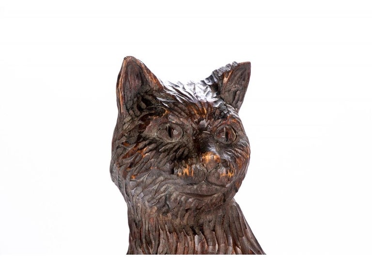 A seated cat looks outward with its tail curled around one leg. Carved overall in rough textured surface with square base.
Measures: Height 19 1/2