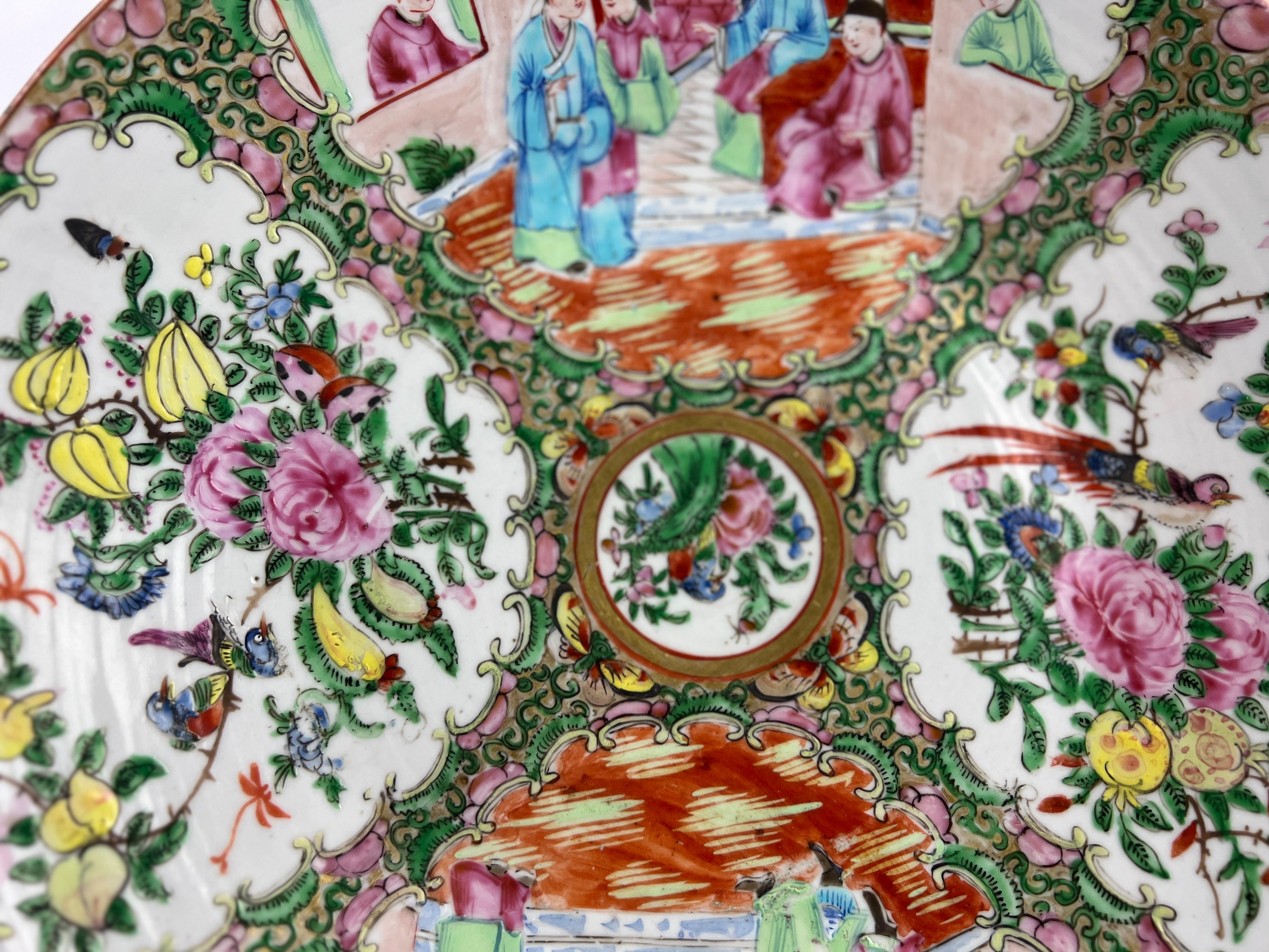 Esta exquisita fuente antigua china con medallón de rosa familiar, de 13,5 pulgadas de diámetro, muestra el intrincado arte y la vibrante paleta sinónimos de la porcelana de exportación de la dinastía Qing. Decorada con un clásico diseño Famille