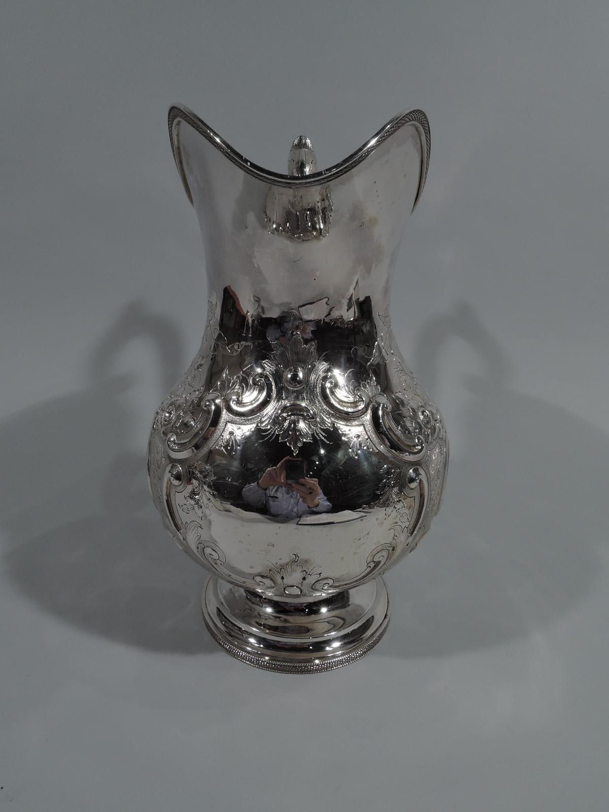 Large coin silver water pitcher. Made by John L. Westervelt in New York City, circa 1850. Baluster with helmet mouth, leaf-capped s-scroll handle, and stepped foot. Chased and engraved ornament. Large strapwork cartouche (vacant), bands of stylized