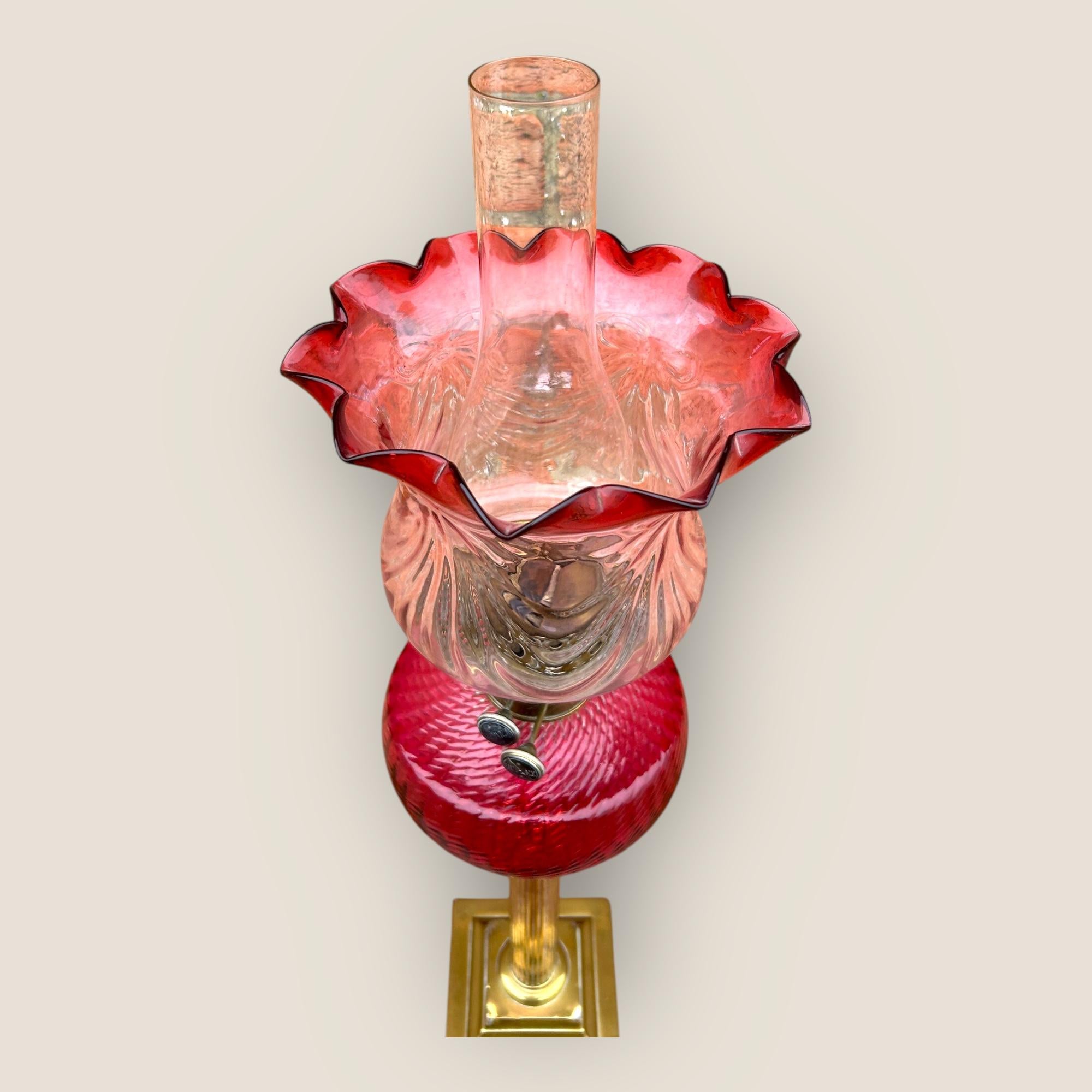 Grande lampe à huile ancienne en laiton canneberge avec un abat-jour en verre canneberge, un réservoir en verre canneberge, une colonne corinthienne en laiton sur une base en laiton.