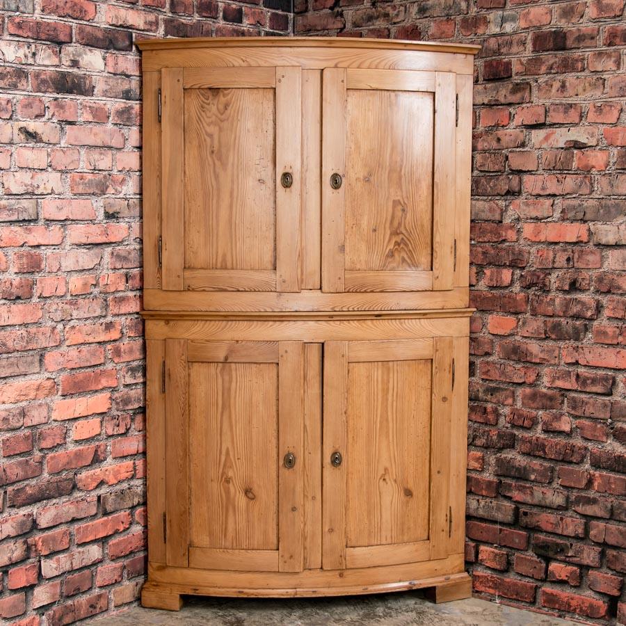 The lovely appeal of this tall bow front corner cabinet is due to the elegant Danish styling and rich patina of the aged pine. The cabinet is made in two sections, both with large bowed paneled doors. Behind the doors are a series of shelves, 3