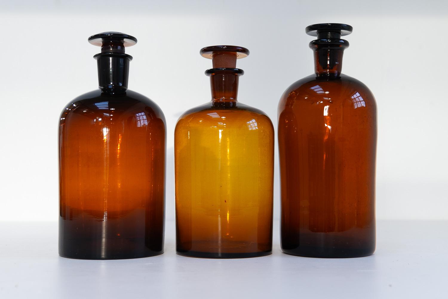Grands flacons anciens en verre de pharmacie danoise, années 1900. Ensemble de 3.

Ensemble de trois grands flacons d'apothicaire soufflés à la main en verre ambré brun/doré avec bouchons.

Taille des bouteilles : 
Diamètre 12,5 cm, hauteur  30.5