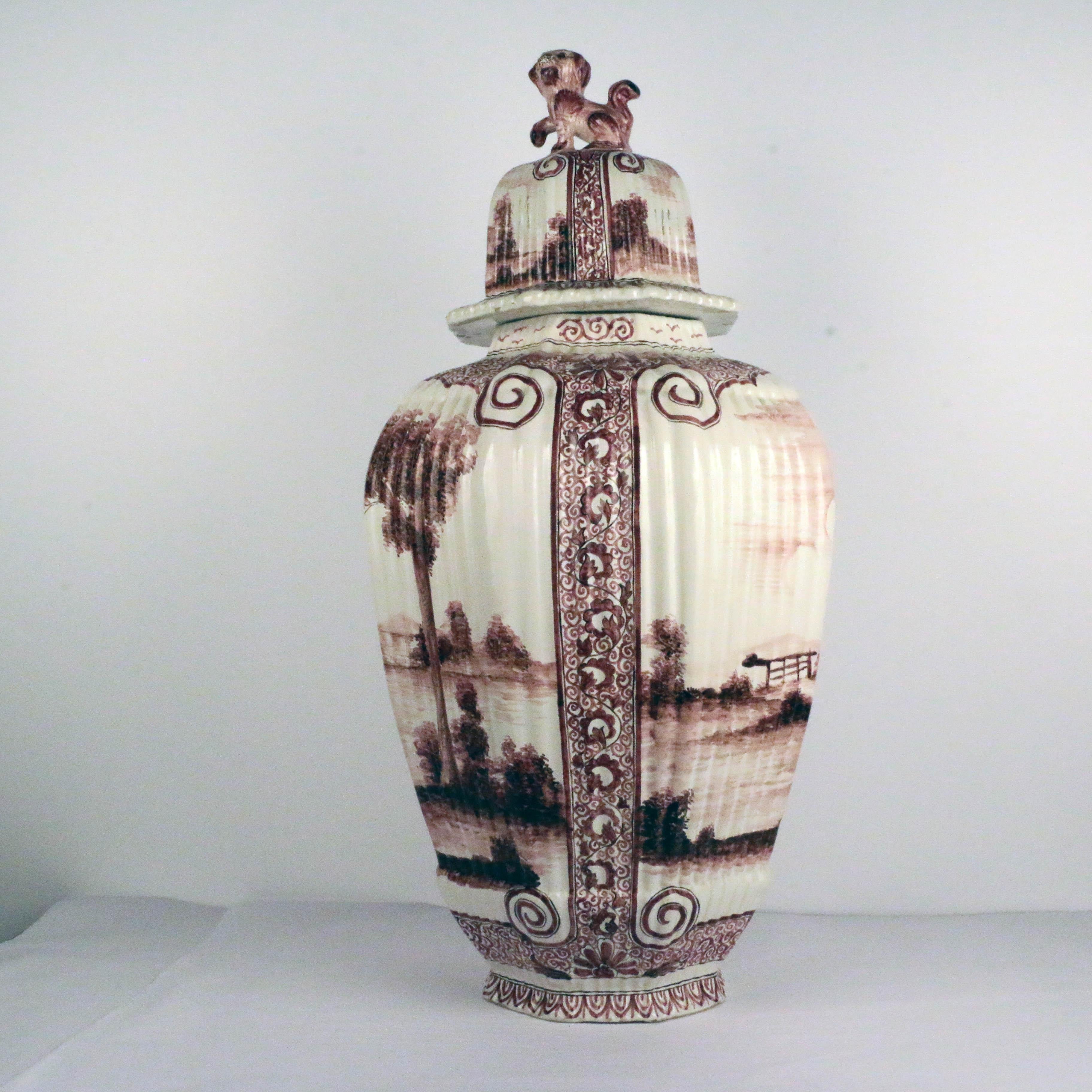 This large covered ginger jar is of tapering octagonal form. Each panel is ribbed and the whole is freely hand-painted in manganese with extensive bucolic landscapes within stylized floral borders. The cover, which continues the motif, has a