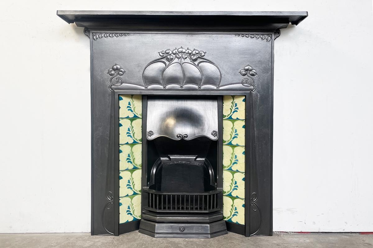 A good example of a large antique Edwardian Art Nouveau cast iron combination fireplace. Dated and produced between 1906-1910. Complete with a set of original book-matched antique Art Nouveau tiles.

Pictured an original cast iron overmantle mirror,