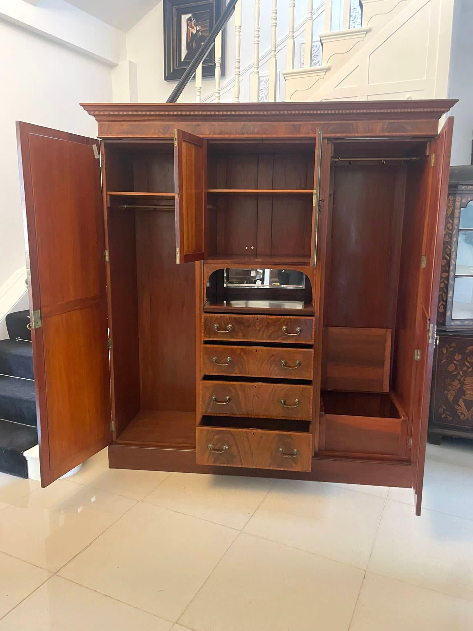 Large antique Edwardian quality mahogany marquetry inlaid wardrobe having a shaped figured mahogany cornice with satinwood inlay above a pair of quality marquetry inlaid doors opening to reveal a storage compartment, bevel edge mirror and 4 figured