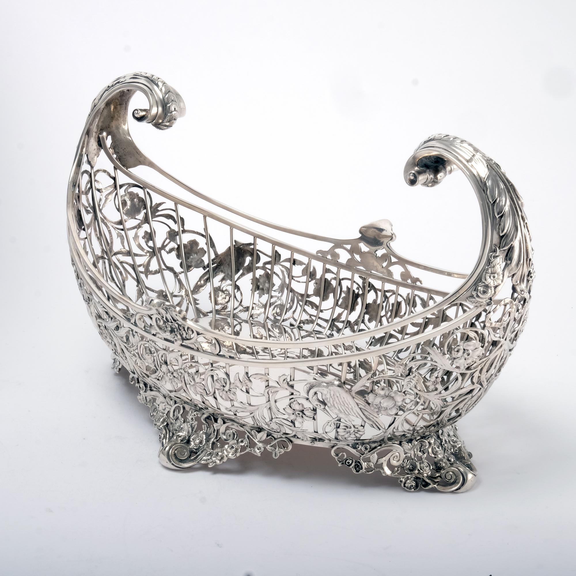 This wonderful and fine-quality Edwardian silver fruit basket, is oval in form with flying leaf-cap scroll handles. The beautiful wirework sides are abundantly adorned with cast bird, leaf and flower decorations. It is a particularly heavy example