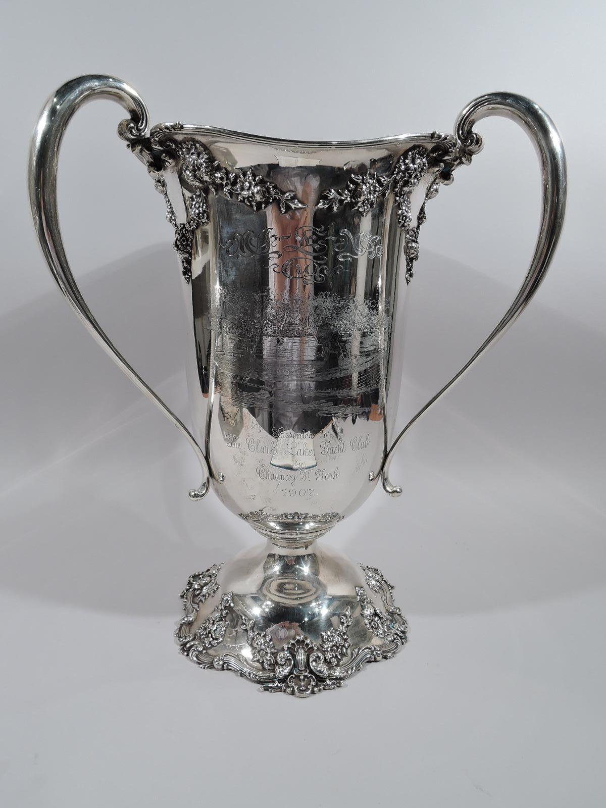 Turn-of-the-century Edwardian sterling silver loving cup. Made by Redlich in New York. Tall urn with three high-looping handles and domed foot. Garland applied to urn top and flowers and shells applied to foot. Rims reeded.
On front are