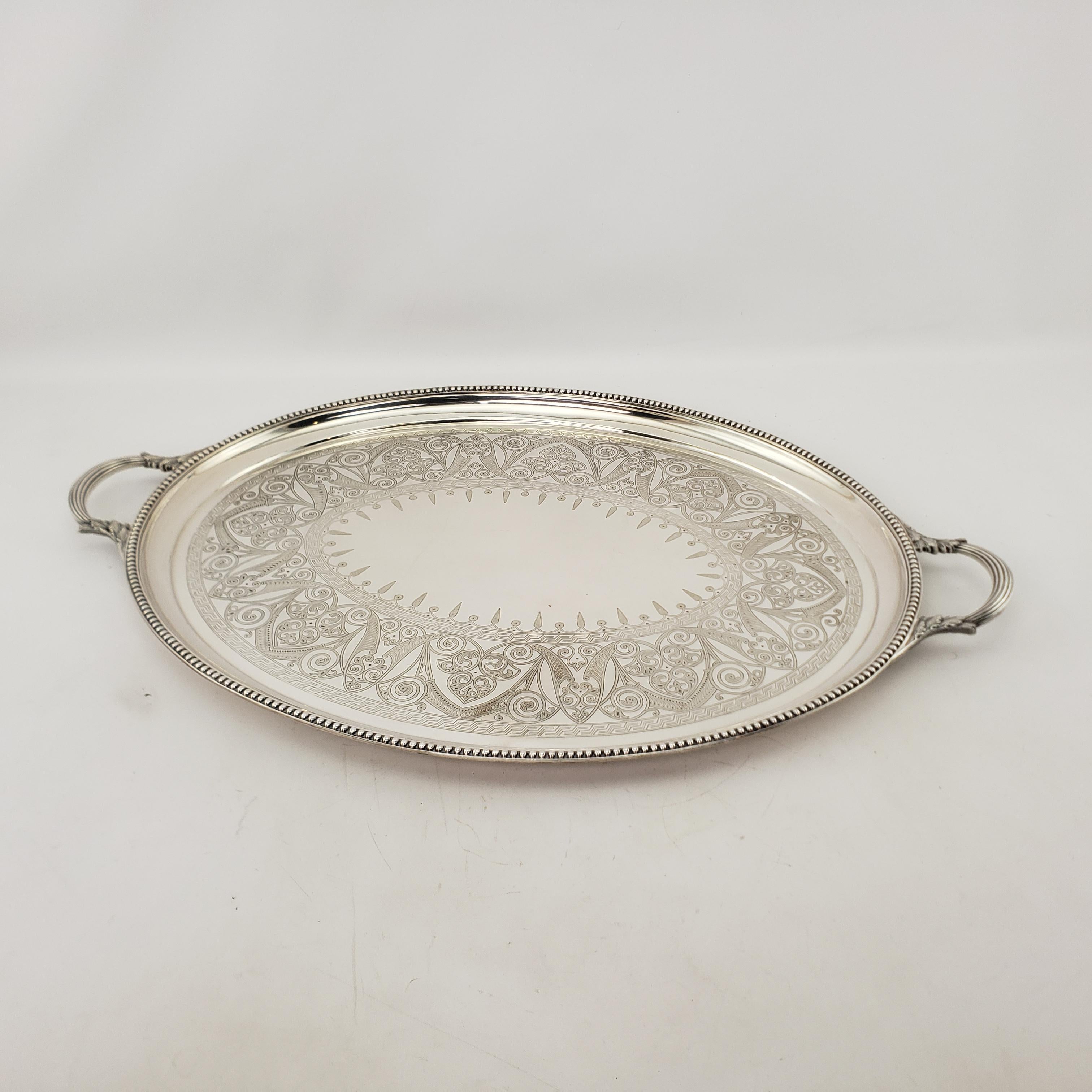This large antique oval serving tray was made by the well known Elkington Co. of England in approximately 1920 in an Edwardian style. The tray is composed of silver plate over copper and has a beaded edge with ornate stylized floral engraved