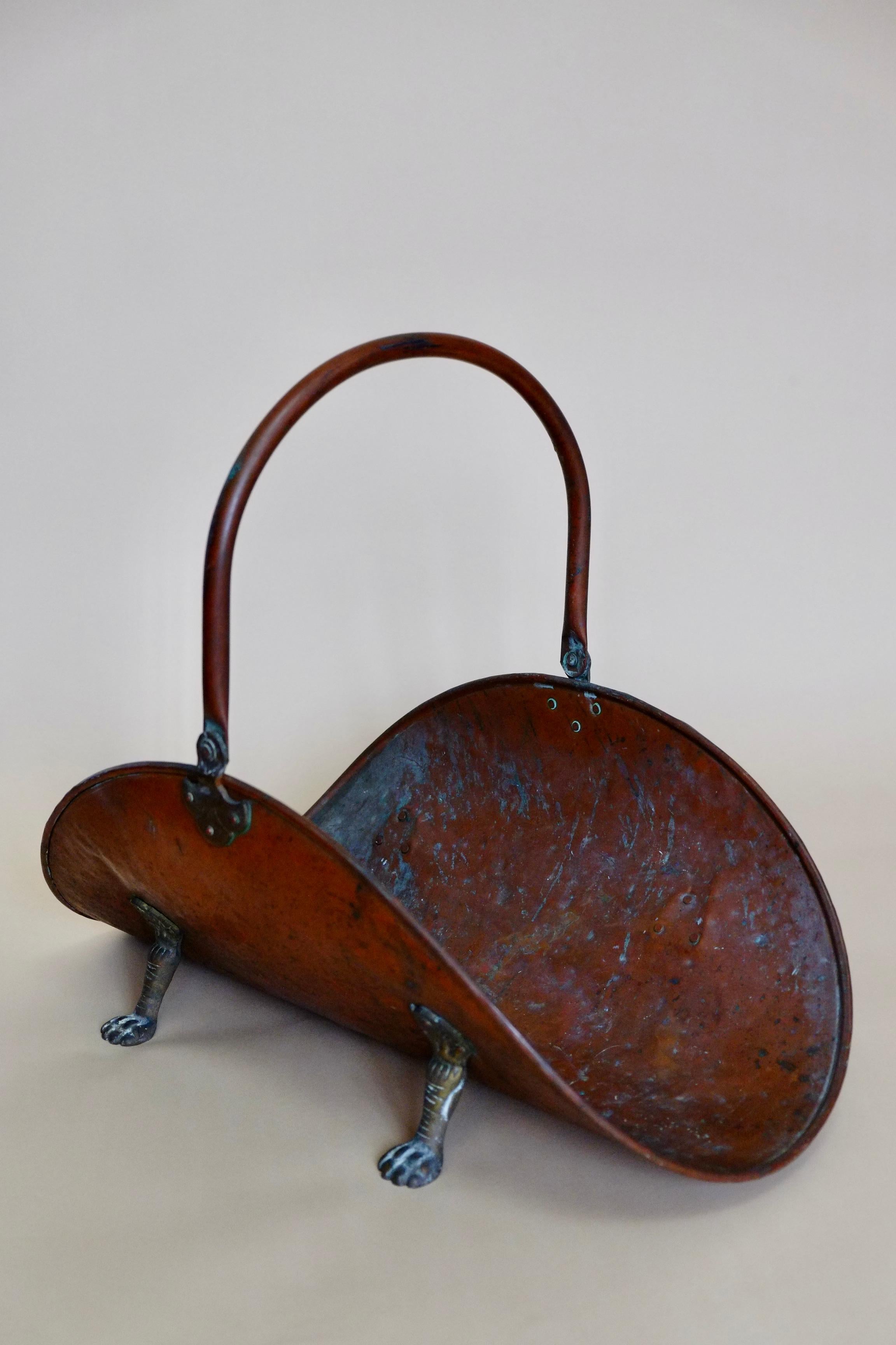 Extra large copper log holder. England circa 1920's. The most beautiful antique piece made in hammered copper sheet with brass details. The log holder has a beautiful curved oval shape and stands on small brass paw feet. There is a long foldable