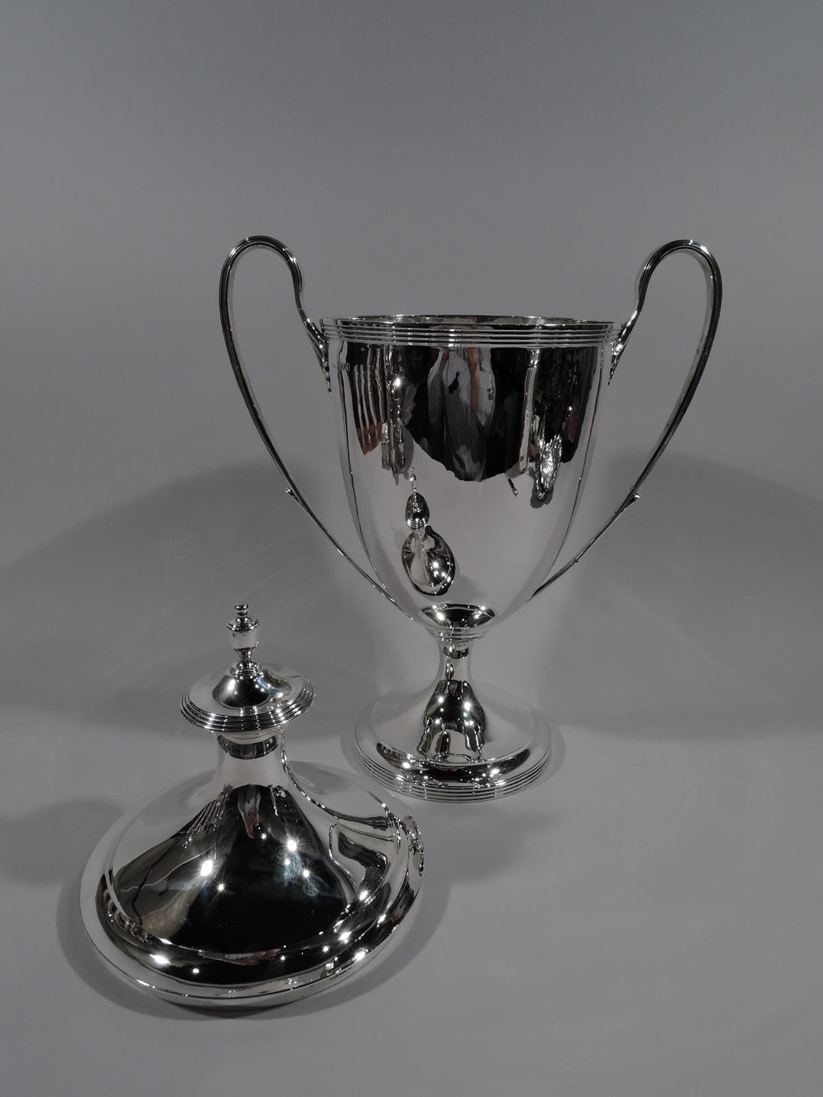 Large Edwardian Classical sterling silver trophy cup. Made by Lionel Alfred Crichton in London in 1911. Elegant Amphora with oval bowl on spool stem flowing into raised round foot. High-looping side handles with leaf mounts. Cover double domed with