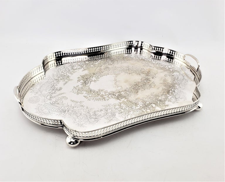 This large silver plated gallery serving tray was made by Maple & Co. of London, England and dates to approximately 1900 and done in a Victorian style. The tray is done in a serpentine shape with ornate stylized floral decoration on the surface of