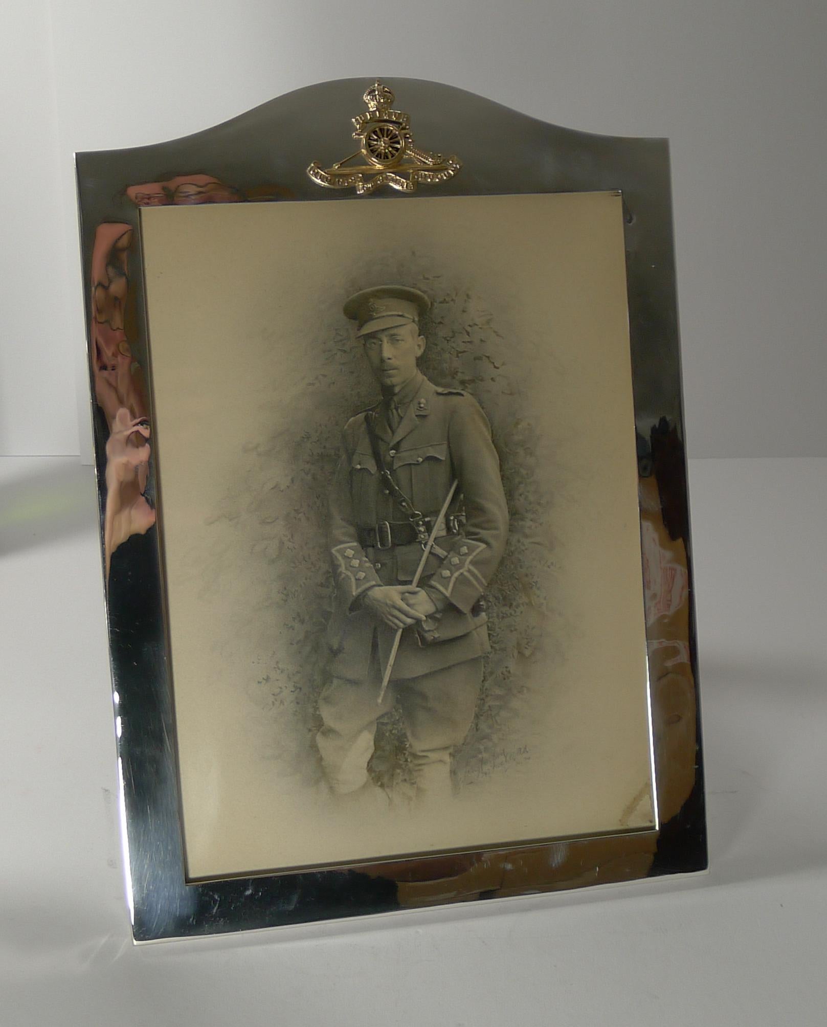A large and grand silver plated photograph frame with military / Royal Artillary interest dating to c.1910.

The top of the frame is mounted with a gilded Royal Artillary cap badge with the motto 