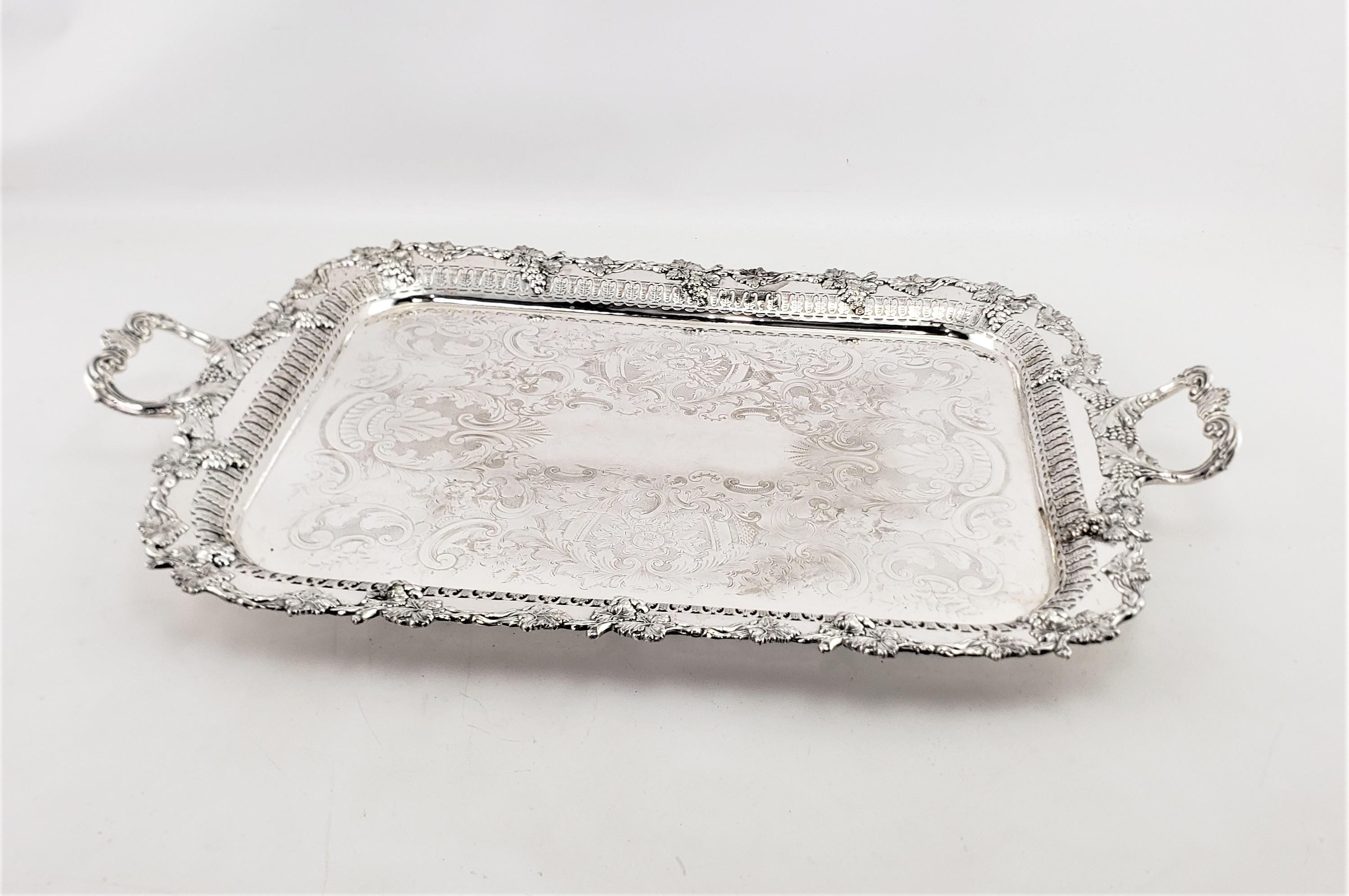 This large antique silver plated rectangular serving tray originates from England and dates to approximately 1900 and done in a Victorian style. The tray is ornately decorated with an applied grape and leaf which is accented on the handles. The
