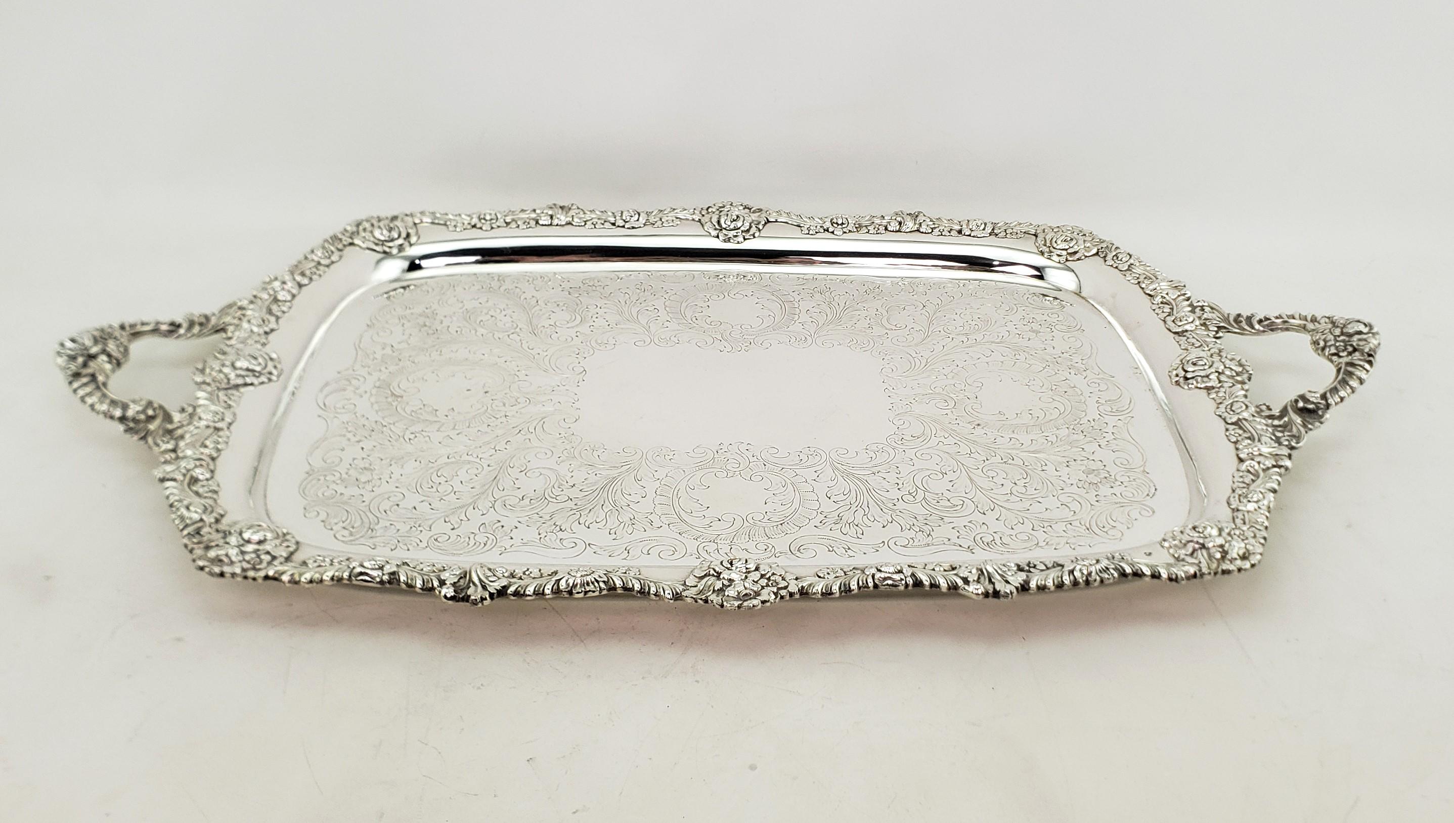 This very large antique serving tray is hallmarked by an unknown maker and originated from England and dates to approximately 1920 and done in a Victorian style. The tray is composed of silver plate and features a very ornate applied floral