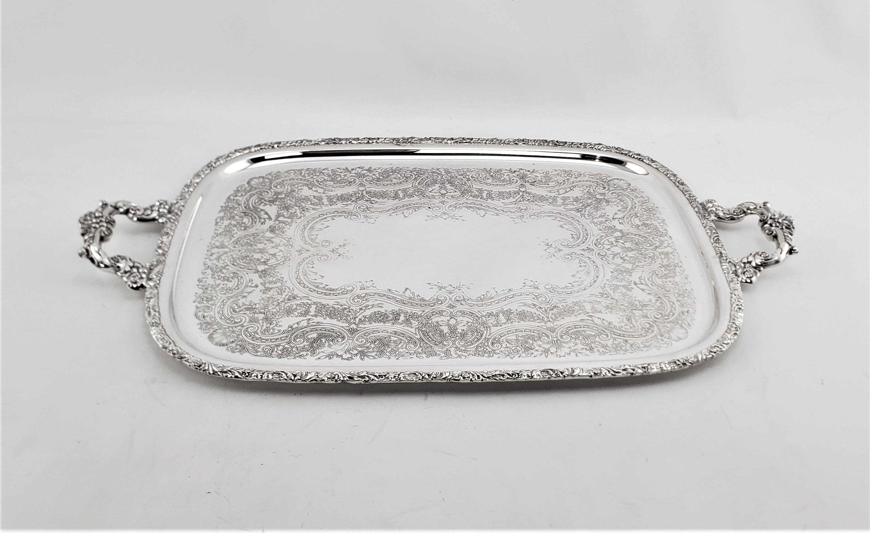 This large silver plated serving tray was made by the International Silver Co. or England is approximately 1920 in a Victorian style. The surface of the tray is ornately engraved with stylized scrolling leaf, and accented by elaborately cast