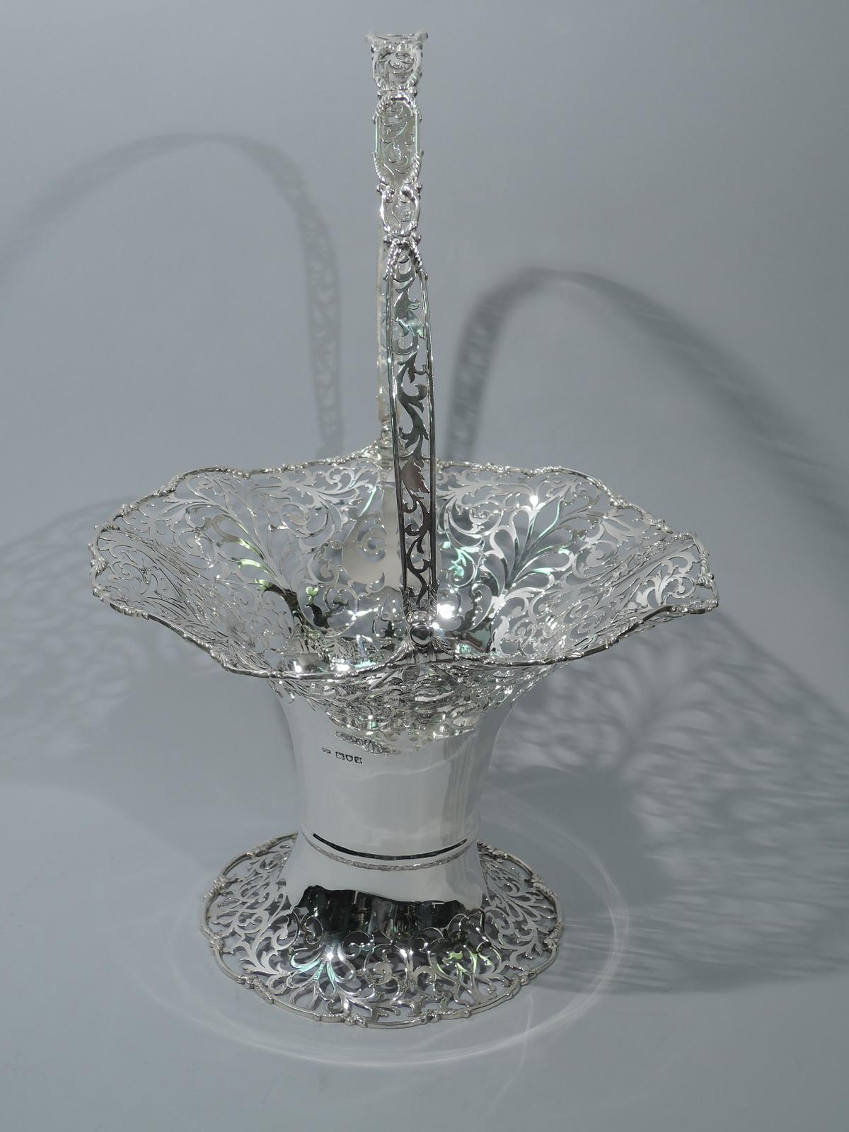 George V sterling silver basket. Made by Mappin & Webb in London in 1911. Cylindrical and girdled body with raised and spread foot, flared and scrolled rim, and swing handle. Body is solid with ornamental piercing at top and bottom as well as on