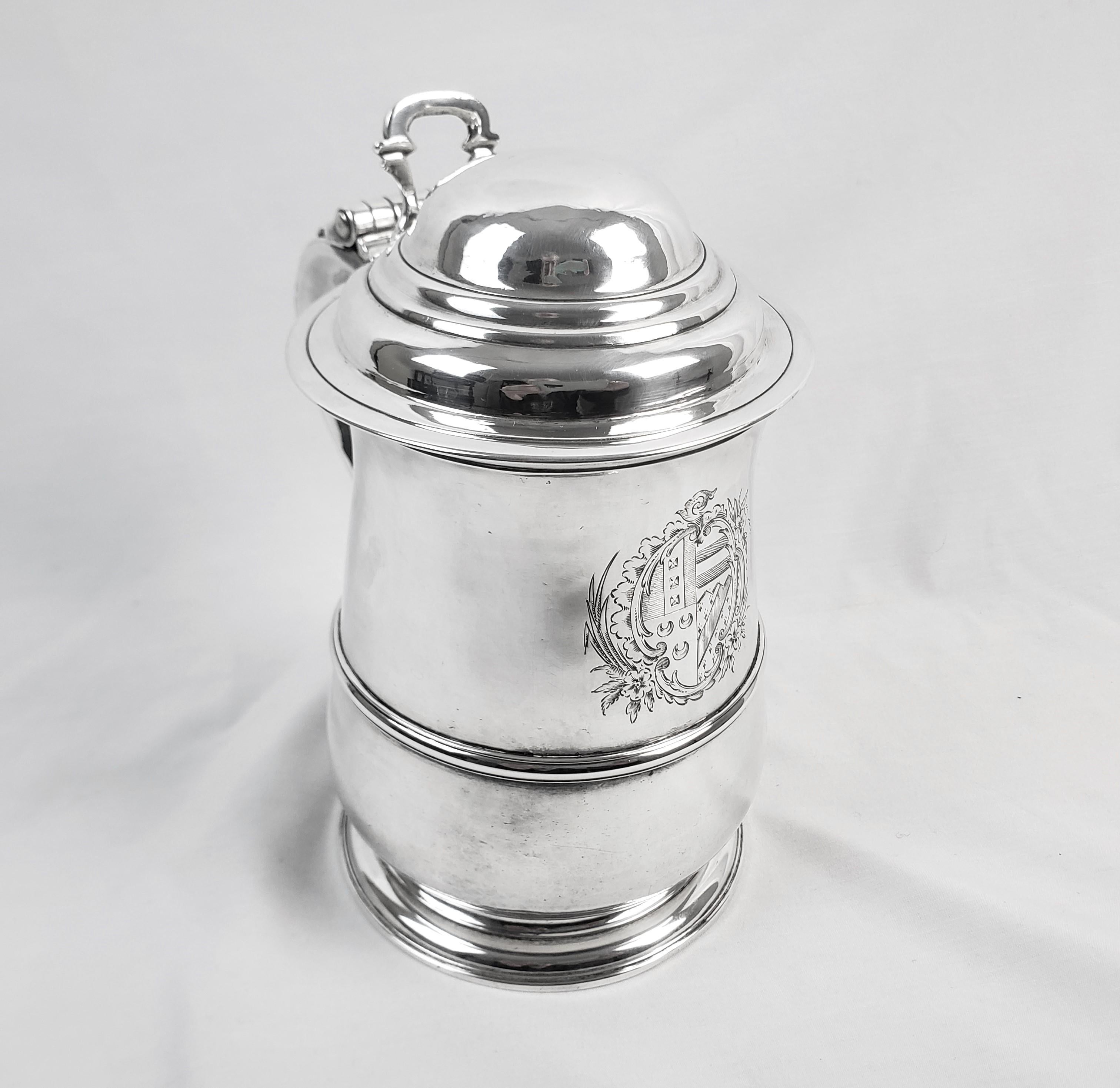 This large and substantial antique tankard is hallmarked by an unknown maker and originated from England, dating to approximately 1740 and done in the period George 3rd style. The tankard is composed of sterling silver with an engraved crest on the