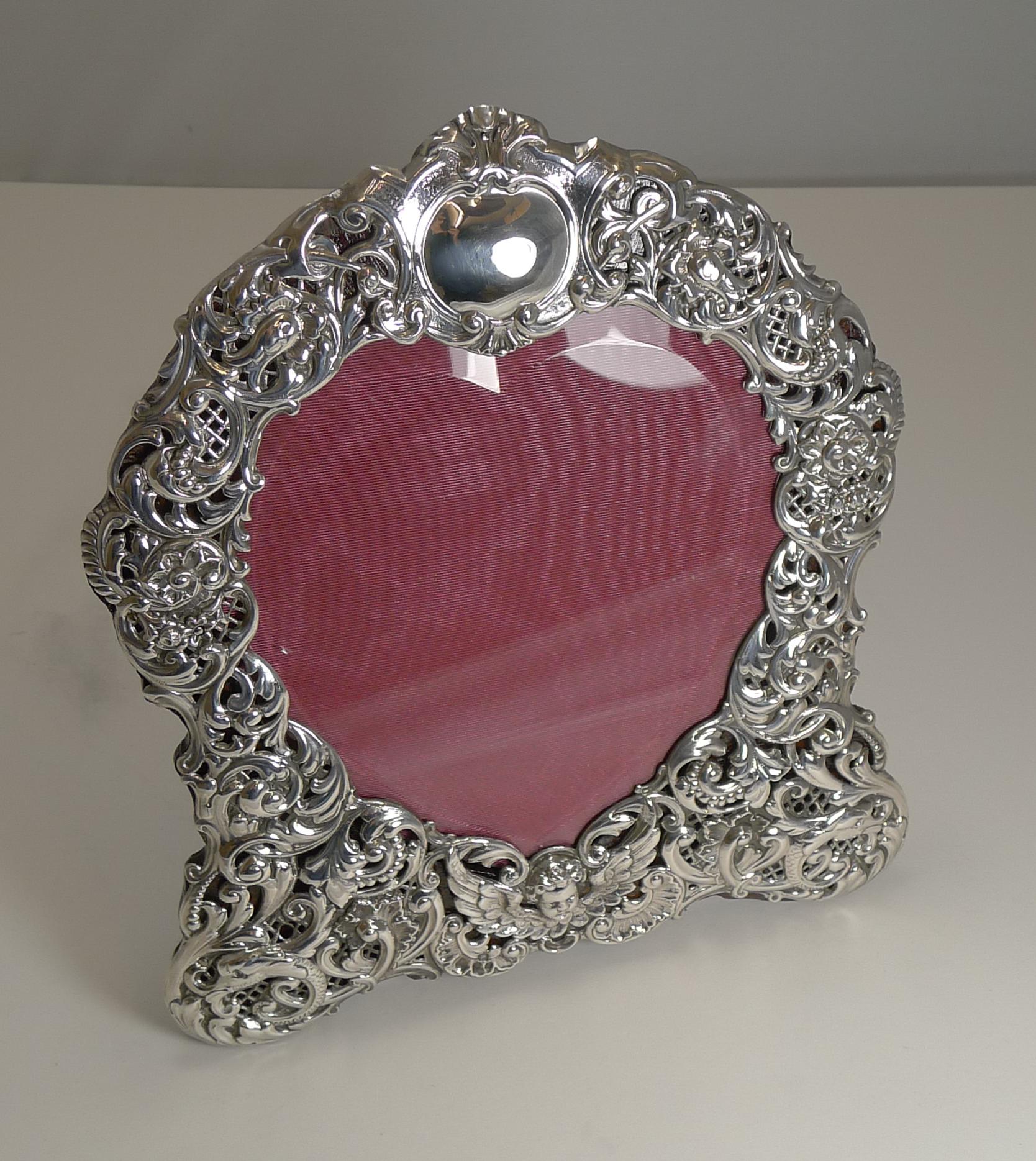 A grand large heart shaped photograph frame made from English sterling silver with intricate pierced or reticulated work incorporating Dolphins on either 