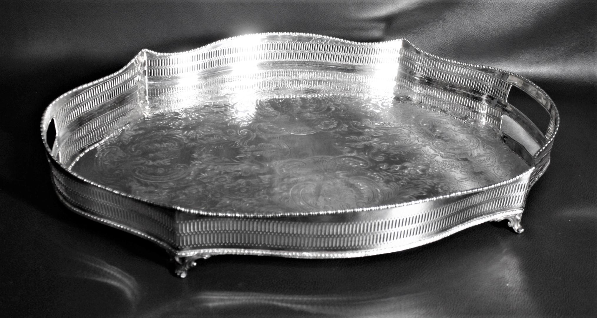 This large serpentine shaped silver plated serving tray was made in Sheffield England in roughly 1910 in the period Edwardian style. This plated tray has a deep gallery with cutout handles on either side and a serpentine shape with four nice tapered