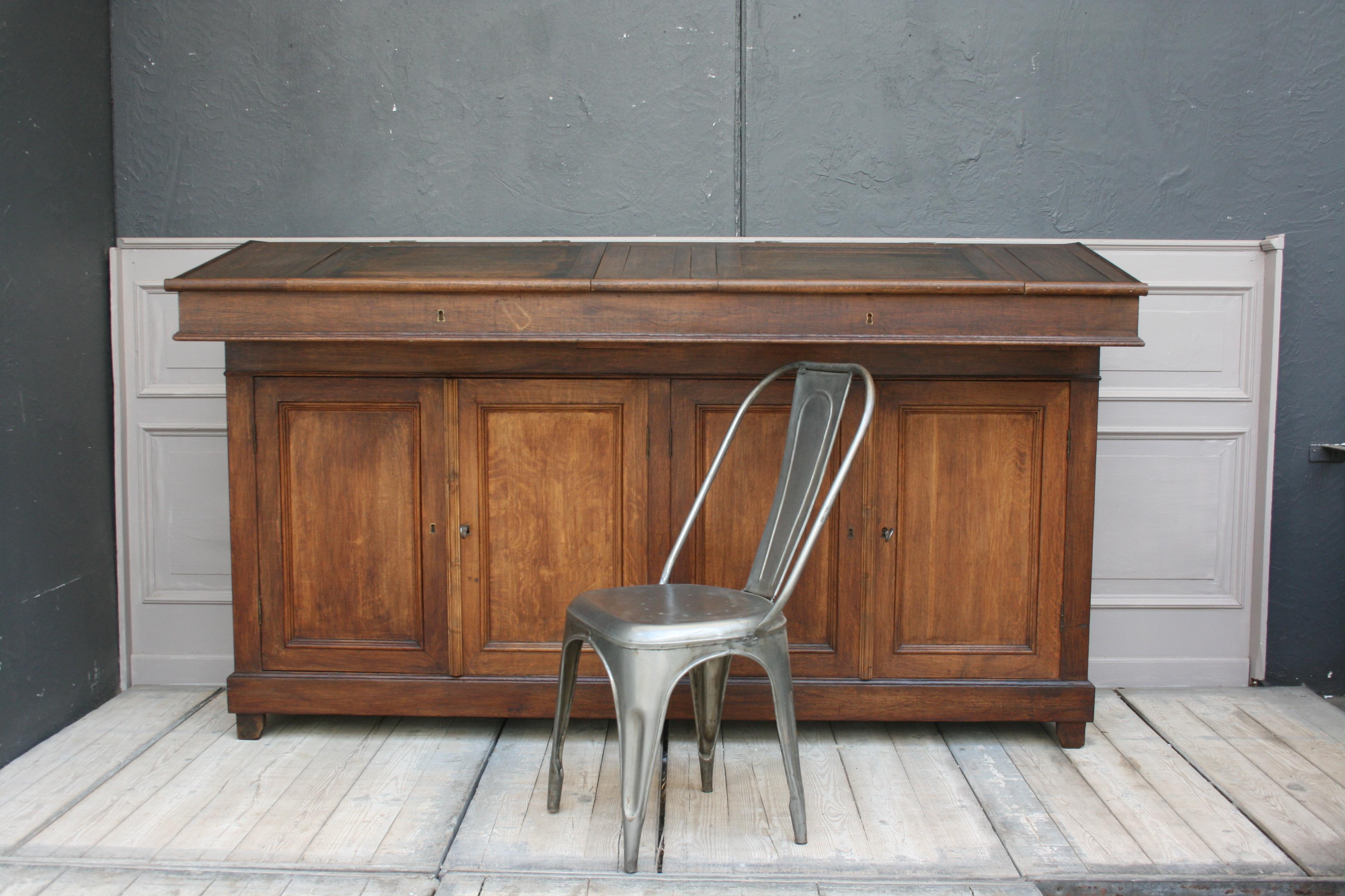 An original old large factory office lectern from France from circa 1880, made of solid oak.
It consists of 2 parts, first the lower cabinet with 2 double doors, which can still be locked with the original bar lock, and second the console top with