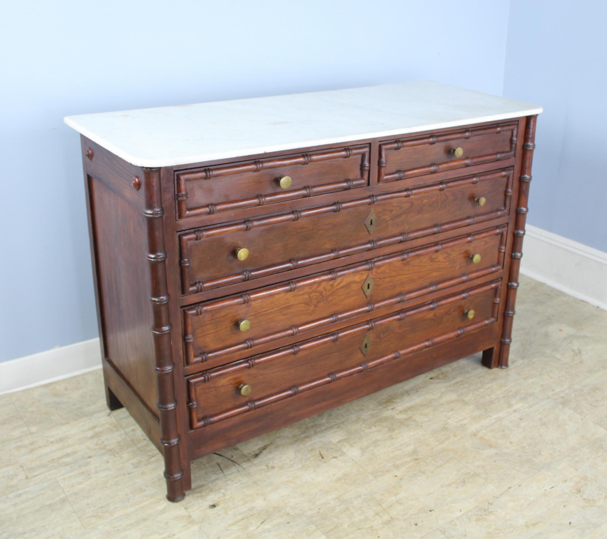 A charming dark pine chest of drawers with faux bamboo columns and mouldings. Classic two-over-three-drawer construction. The interiors of the drawers are clean and the drawers open easily and shut snugly. The marble which is original is fine