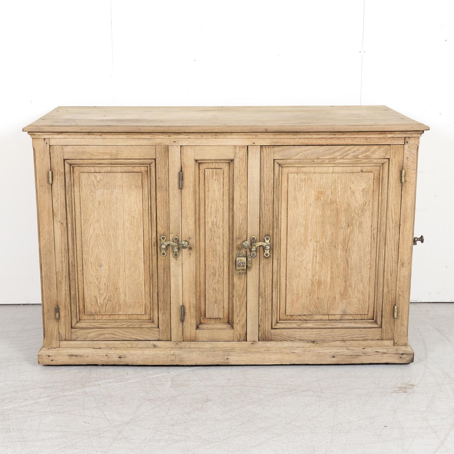 A fabulous large antique French industrial icebox from Normandy in bleached oak, circa 1920s, that is lined with zinc, having three front doors and a single door on the left side, all with original brass hardware. The four panel doors open to reveal