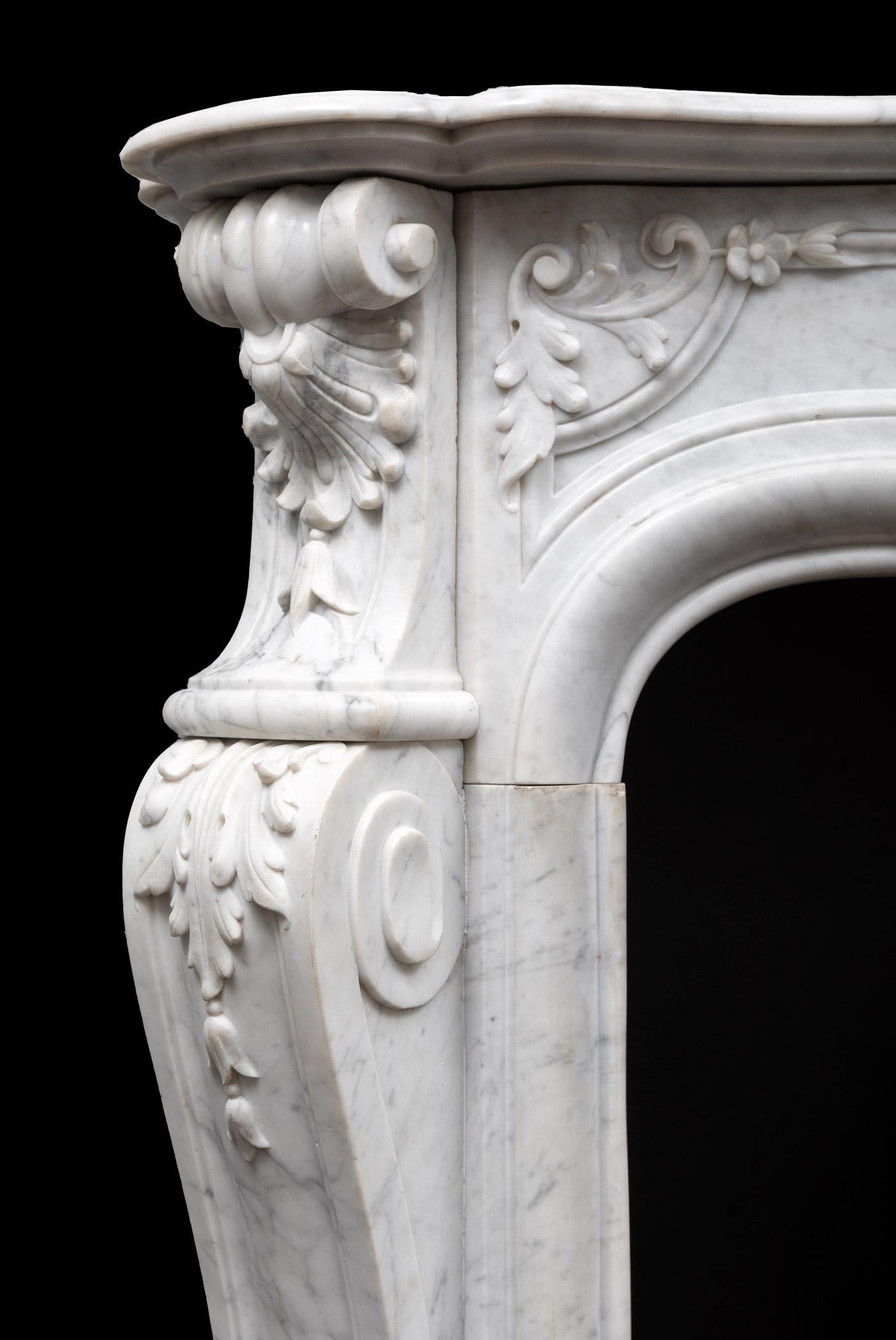A stunning antique French Louis XV Rococo style fireplace carved from Carrara marble. The serpentine shaped panelled frieze is beautifully carved with flowers and foliage emanating from the central scallop shell cartouche. The splayed and carved