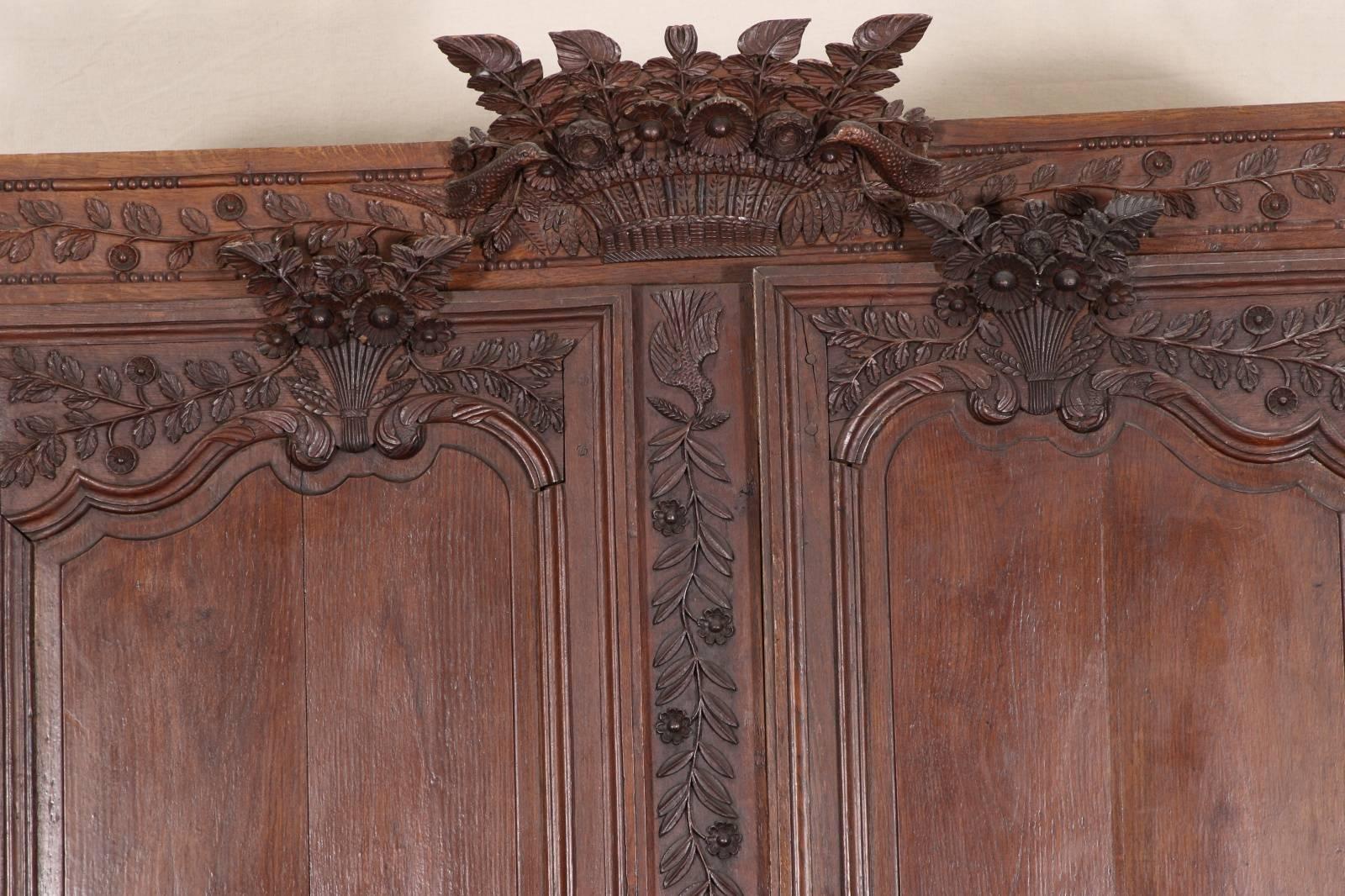 Antique carved French armoire, oak, elaborately carved projecting crest of a floral basket with birds, the doors with tall crests of bunches of flowers on the tops, and roundels of lidded urns in relief on the front. Overall carved bands of