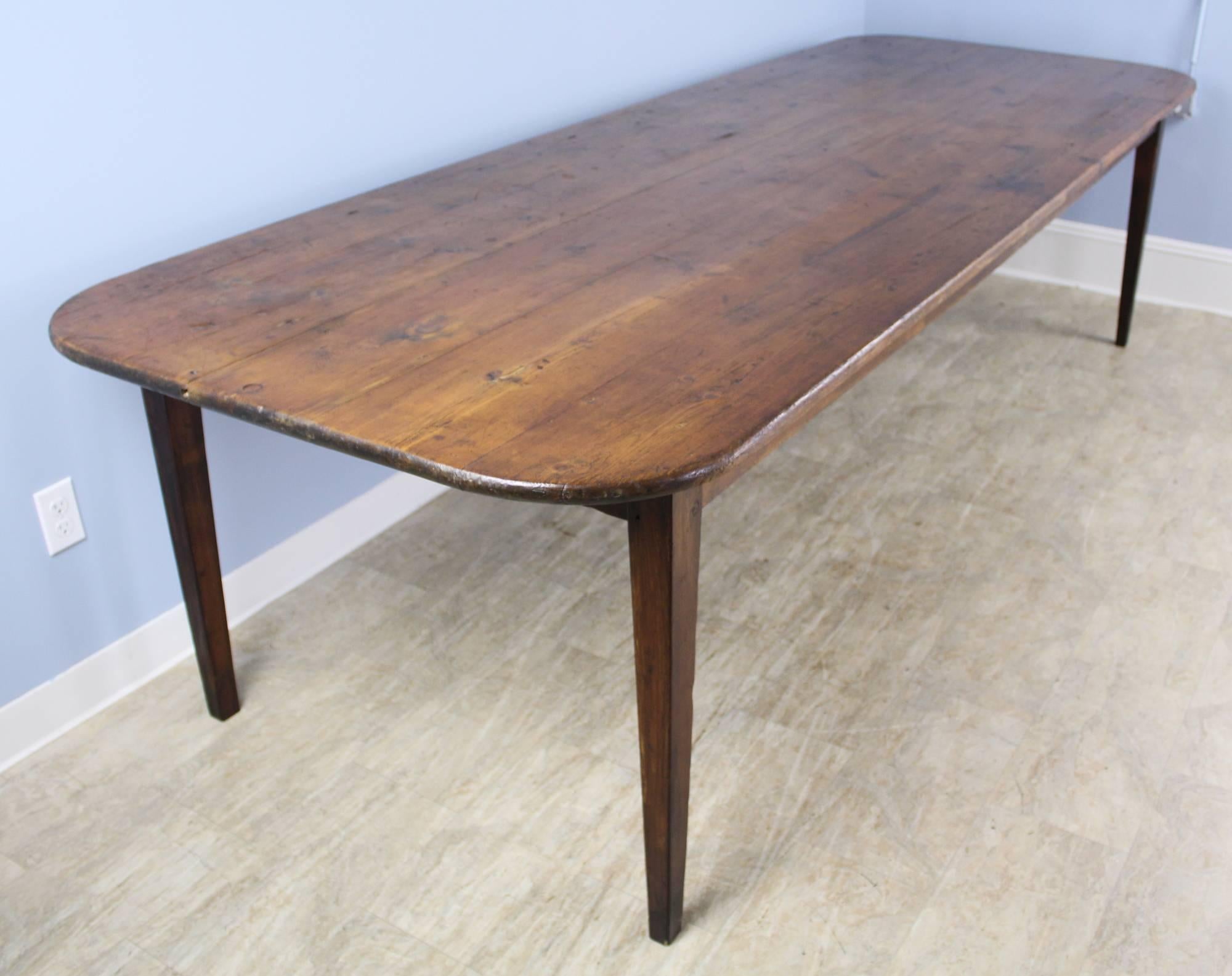 A long and wide country rustic farm table, in rich deep pine, with a lovely patina. Great planking and distress. Very practical rounded corners, and good knee room with a 25.25 inch apron height. Sturdy and offering very good seating for 10-12, at