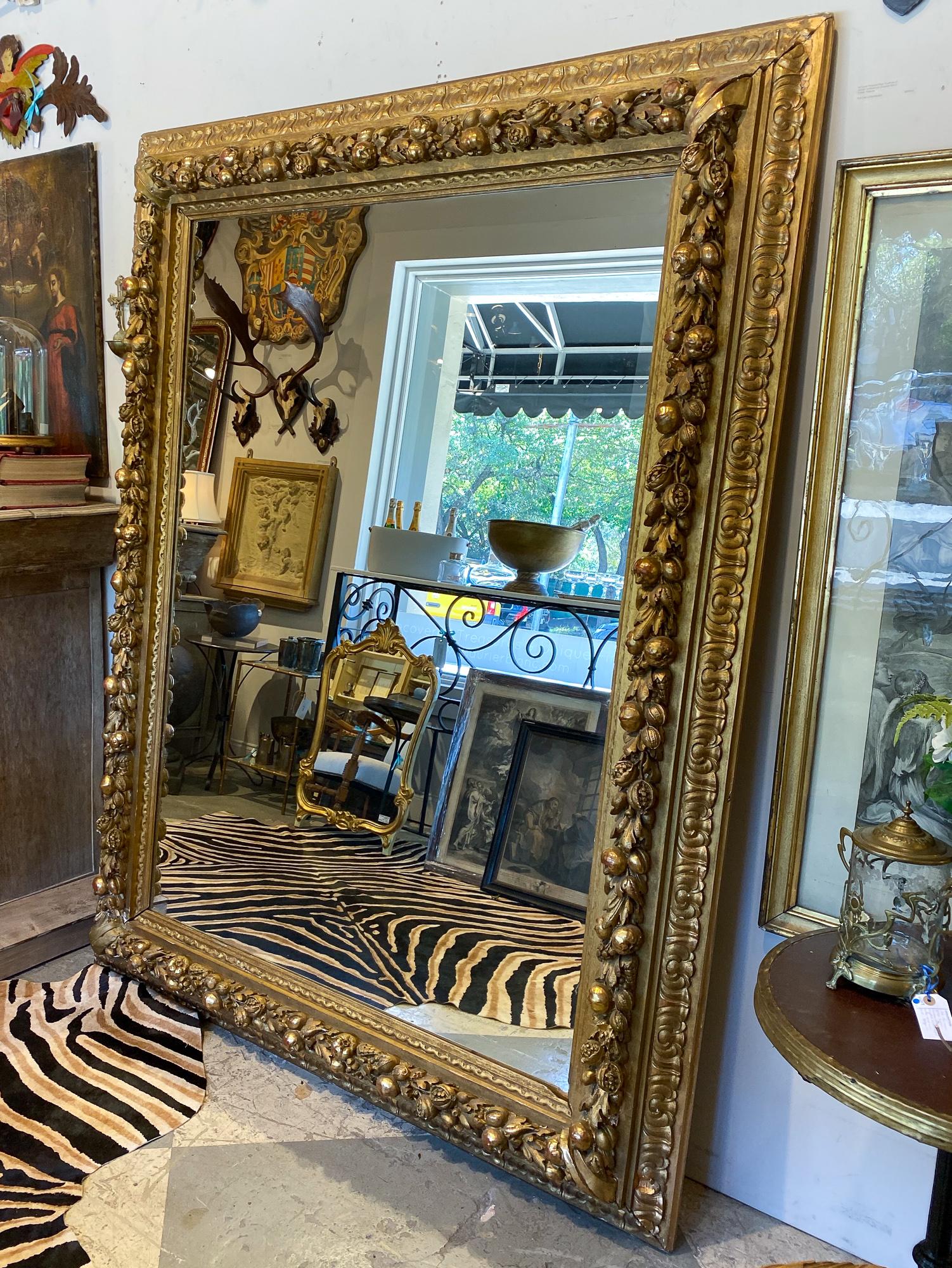 Early French large scale mirror with exquisitely crafted pomegranate, floral and leaf detail in plaster and carved wood with gold gilt detail. Dating to the late 19th century, the mirror measures 61.5