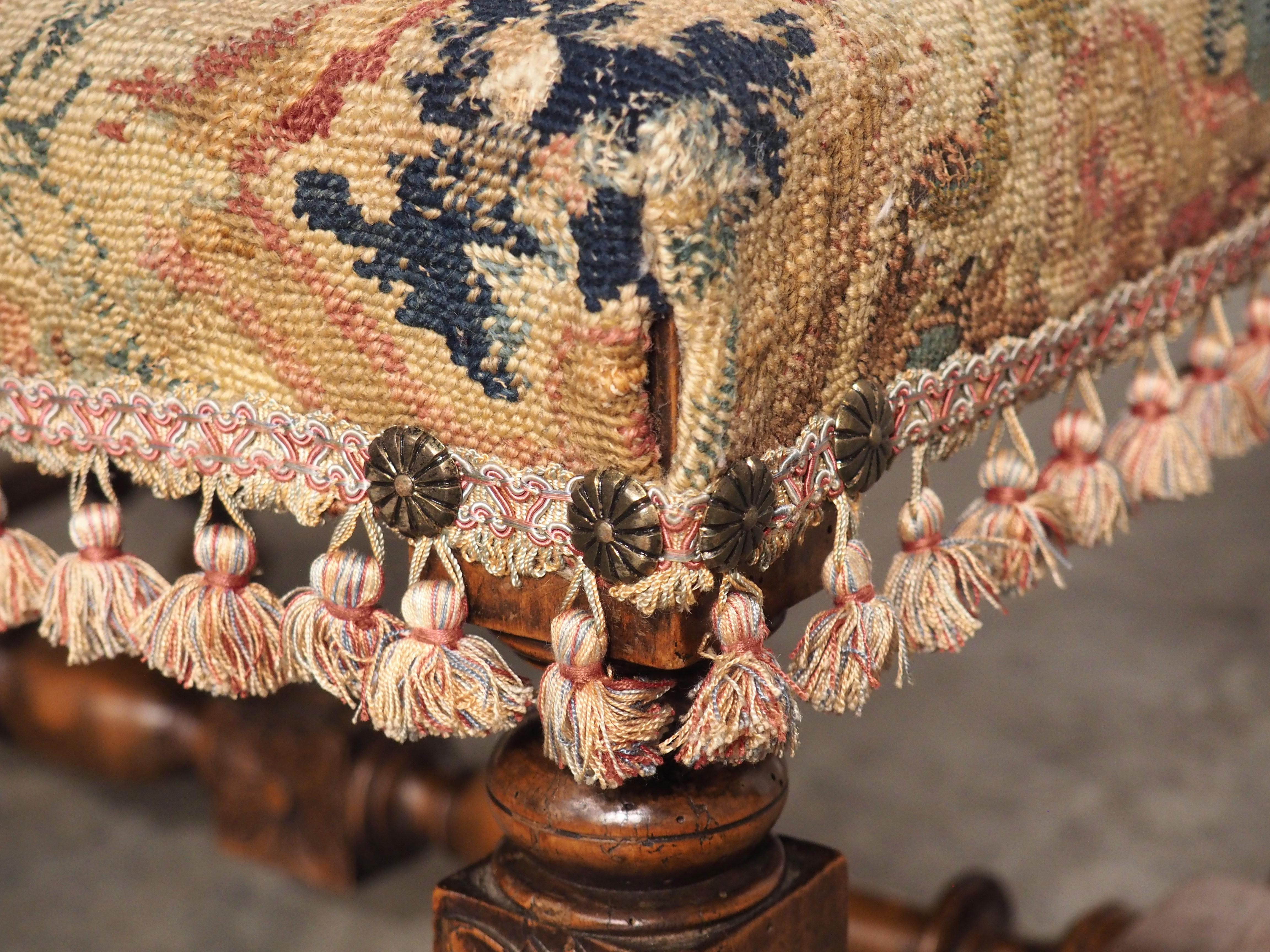 Hand-carved in the style of Louis XIII, this large needlepoint upholstered tabouret is from France, circa 1870. Typical period motifs are noticeable, including the turned H-stretcher on bun feet, daisy-like iron nail heads (four on each corner)