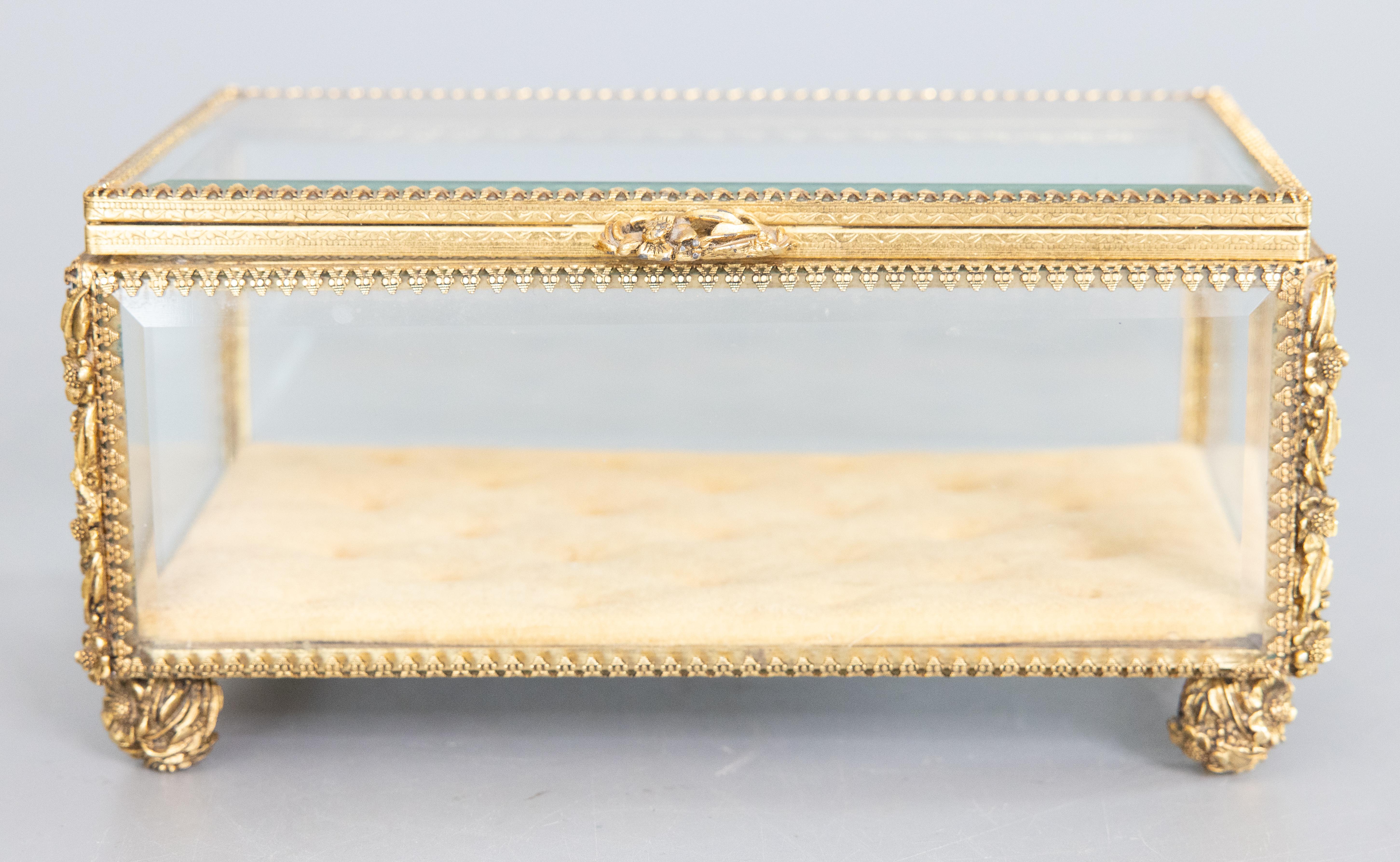 A stunning antique French brass ormolu beveled glass footed jewelry casket or dresser box with hinged lid and lovely flower shaped handle. This fine quality box has the original tufted velvet lining and is a large rectangular design with thick