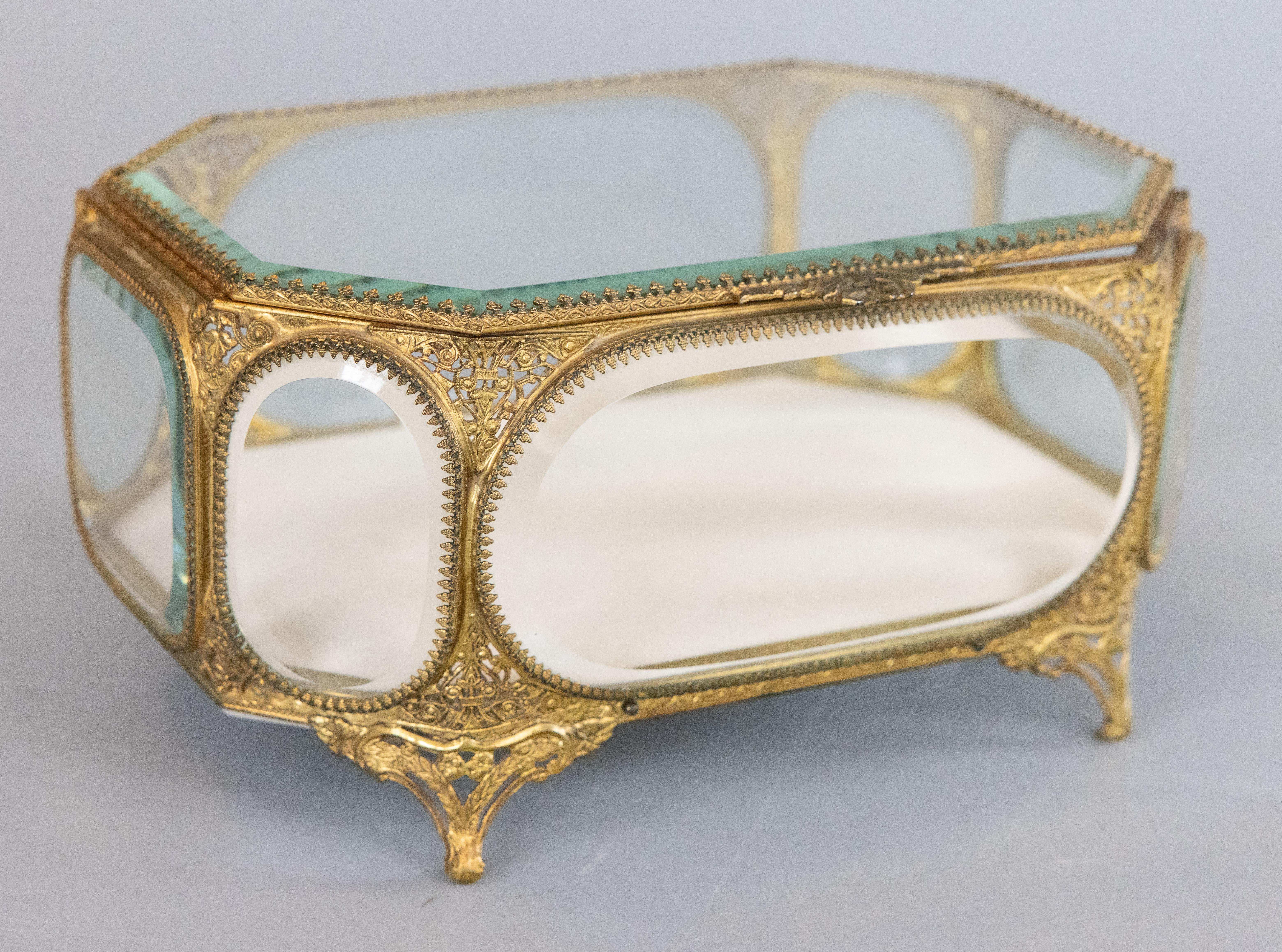 Impresionante cofre o joyero francés antiguo de latón u ormolu con pie de cristal biselado, tapa abatible y preciosa asa en forma de lazo. Esta caja de gran calidad se ha revestido de nuevo con terciopelo marfil y es un raro diseño octogonal de gran