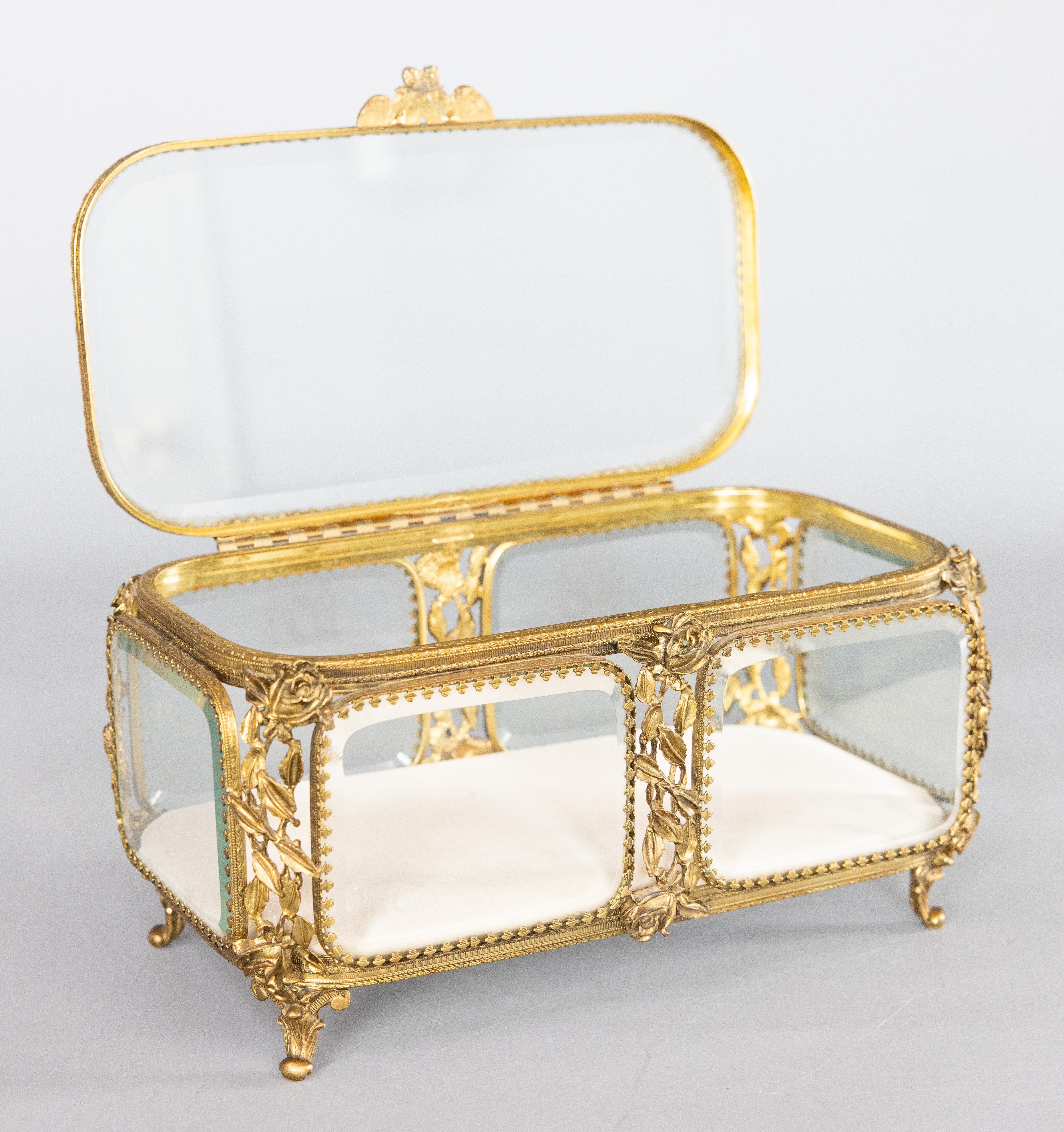 A stunning antique French brass ormolu beveled glass footed jewelry casket or dresser box with hinged lid and lovely flower shaped handle. Newly relined with ivory velvet. This fine quality box has a large rectangular design with thick beveled