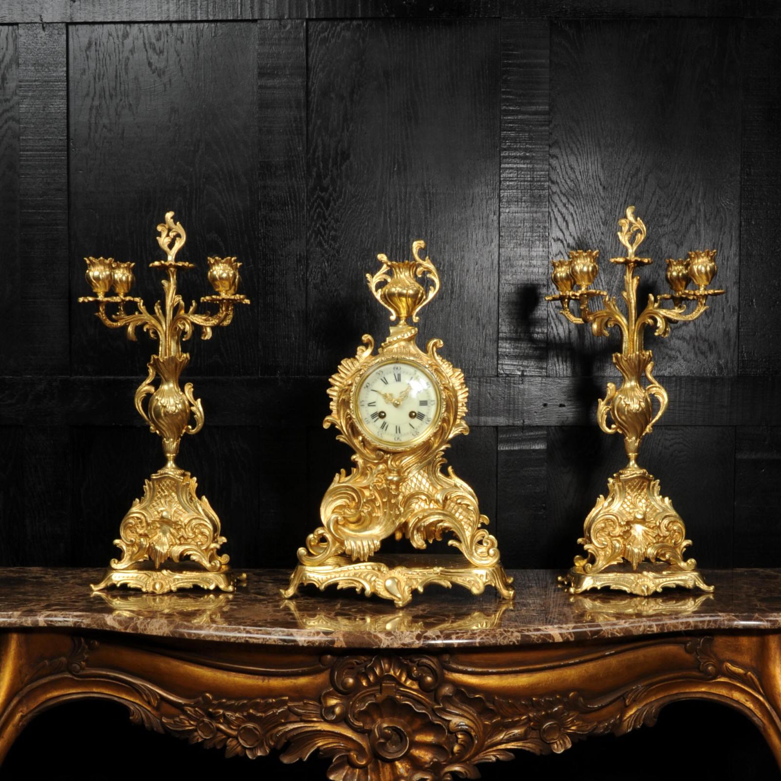 A stunning and large original antique French gilded bronze clock set. It is of the most beautiful Rococo style, waisted case decorated with bold 'C' scrolls, acanthus leaves and standing on an integral base. To the top is a Rococo urn.  Candelabra