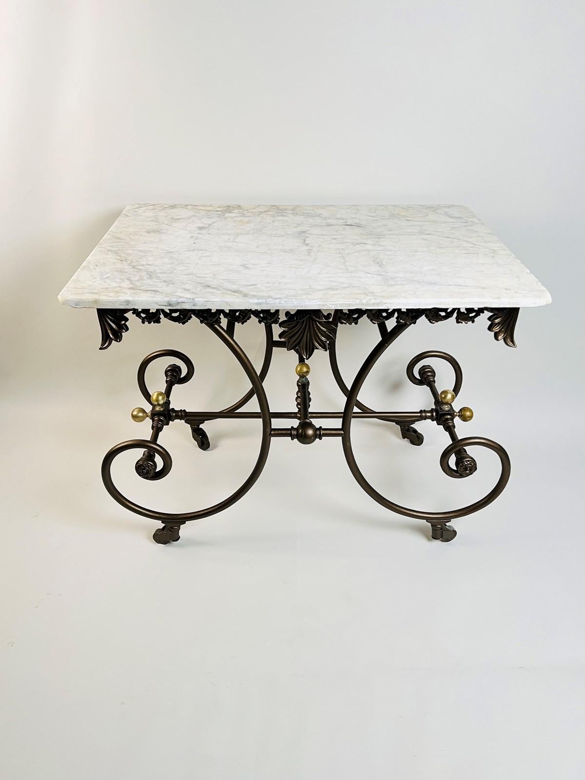 Cette table de boulangerie ou de pâtisserie française ancienne présente un plateau en marbre de Carrare aux angles arrondis, gracieusement placé au-dessus d'un tablier en fer forgé orné de motifs floraux et de vignes en volutes. Le centre et les