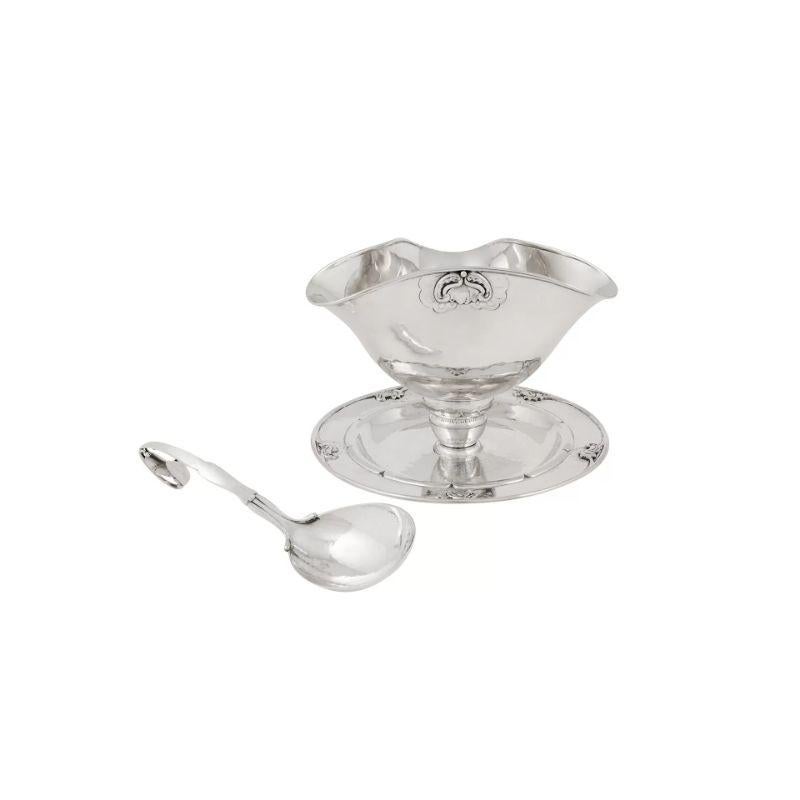 A rarely seen extra large Georg Jensen 830 silver gravy bowl on a fixed saucer, design #328 by Georg Jensen from circa 1919. The bowl is in a tricorn shape and decorated with partially hand-chased and partially applied stylistic floral details. This