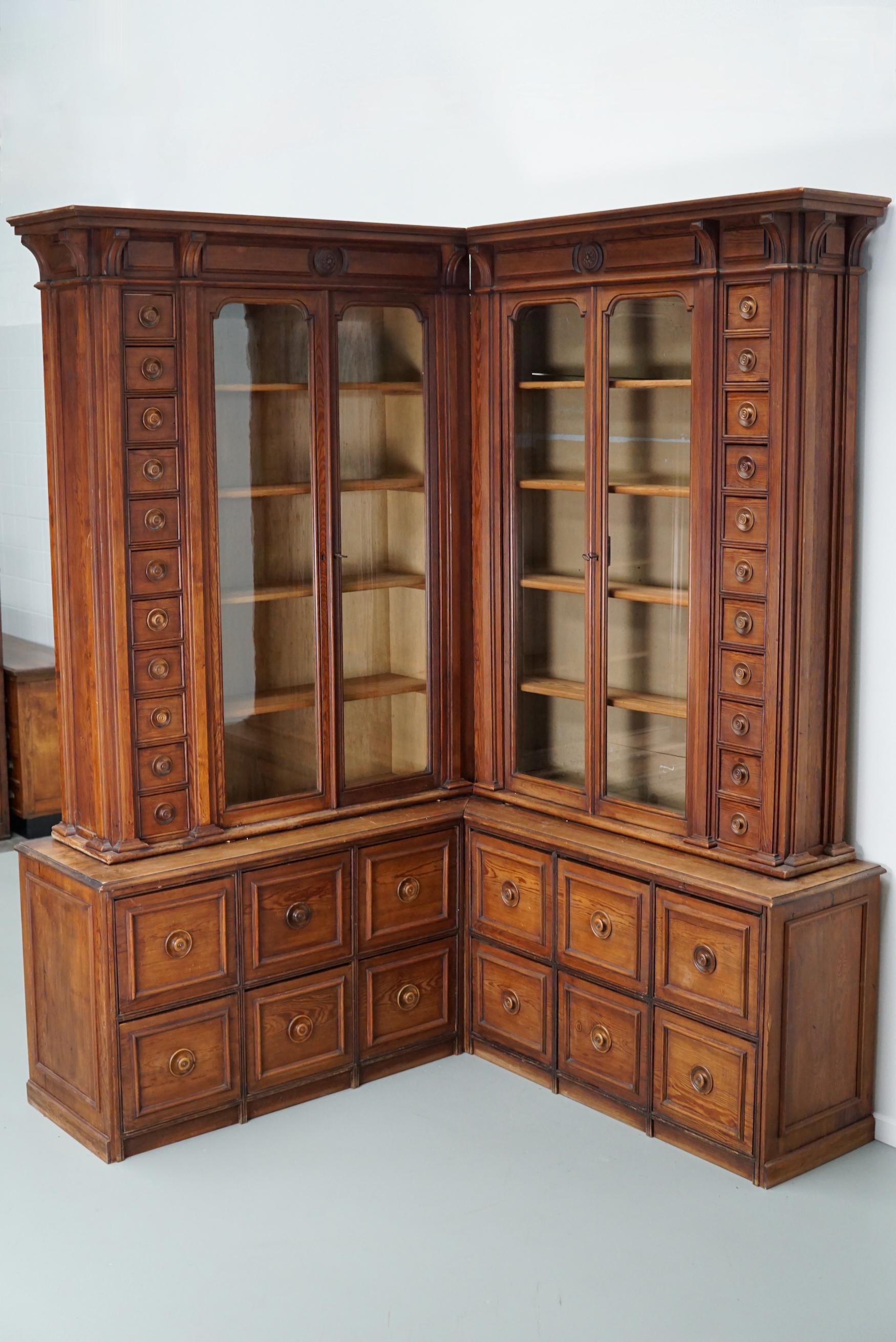 This stunning corner apothecary cabinet was made in Germany around the turn of the century. It features two vitrines with shelves and both small and large square drawers at both ends. It was very well made and retains a nice patine and colour. The