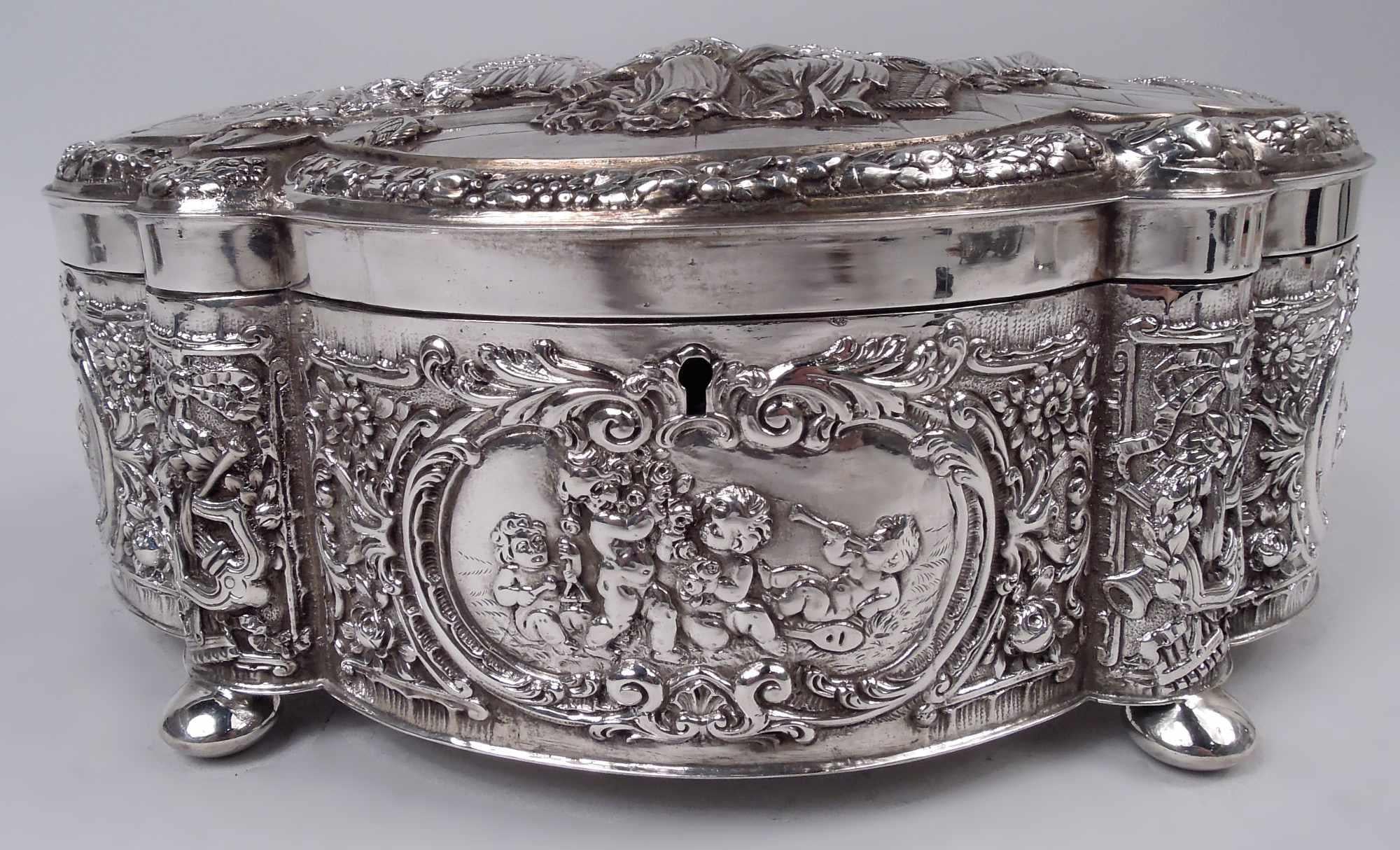 Large German Rococo Classical sterling silver box, ca 1910. Lobed and oval with straight sides and four ball supports; cover hinged and raised. Chased and engraved ornament. On cover top, morally serious scenes: A tambourine-holding woman confronts