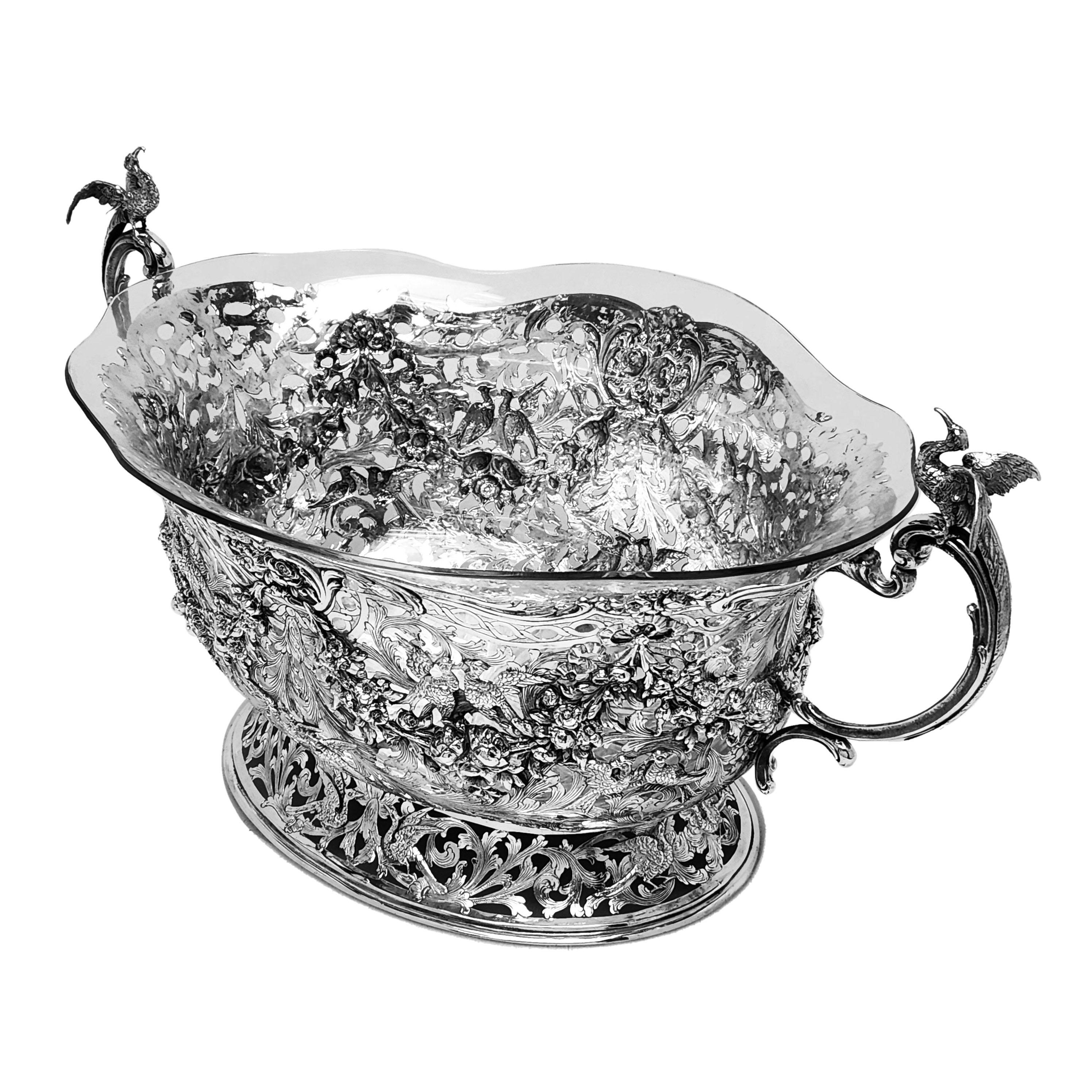 A beautiful Antique German Silver Centrepiece Bowl featuring an ornate chased and pierced design. The design costs of floral and foliate swags and birds on an engraved stylised foliate background. The Bowl has a pair of scroll handles each topped