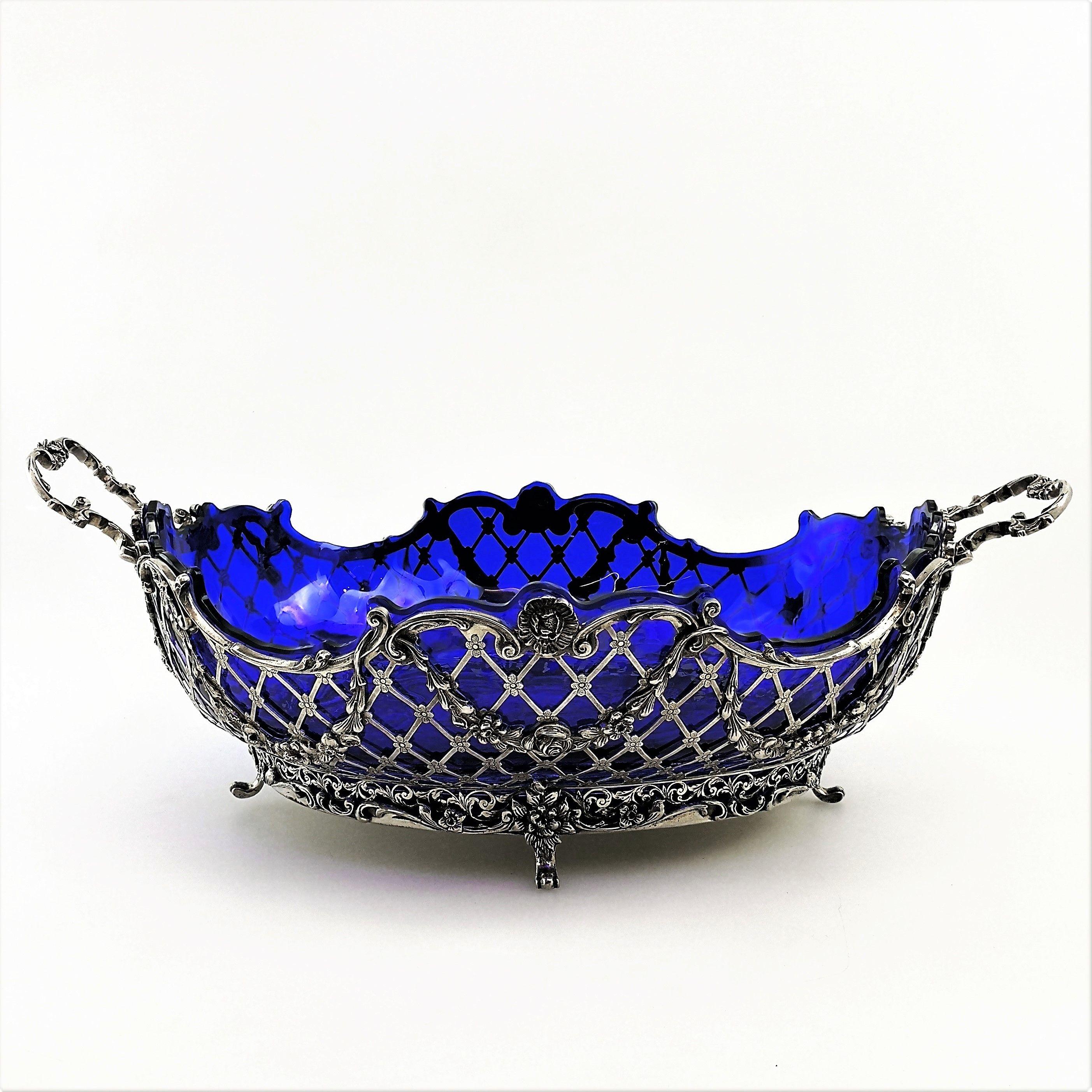 A magnificent Antique German Silver Basket with a deep blue glass liner. This Basket is of particularly large size and features gorgeous pierced and chased details including ornate floral swags along the body of the Basket. The Basket has two shaped