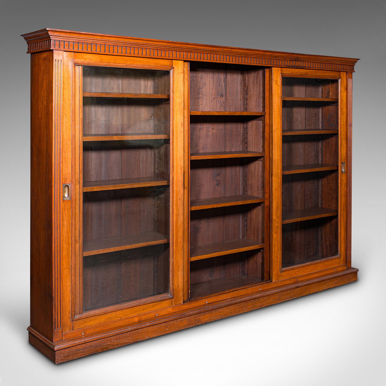 This is a large antique glazed bookcase. An English, grand walnut display cabinet with sliding doors, dating to the late Victorian period, circa 1880. Of exceptional scale and craftsmanship, this library piece would grace the most refined interior