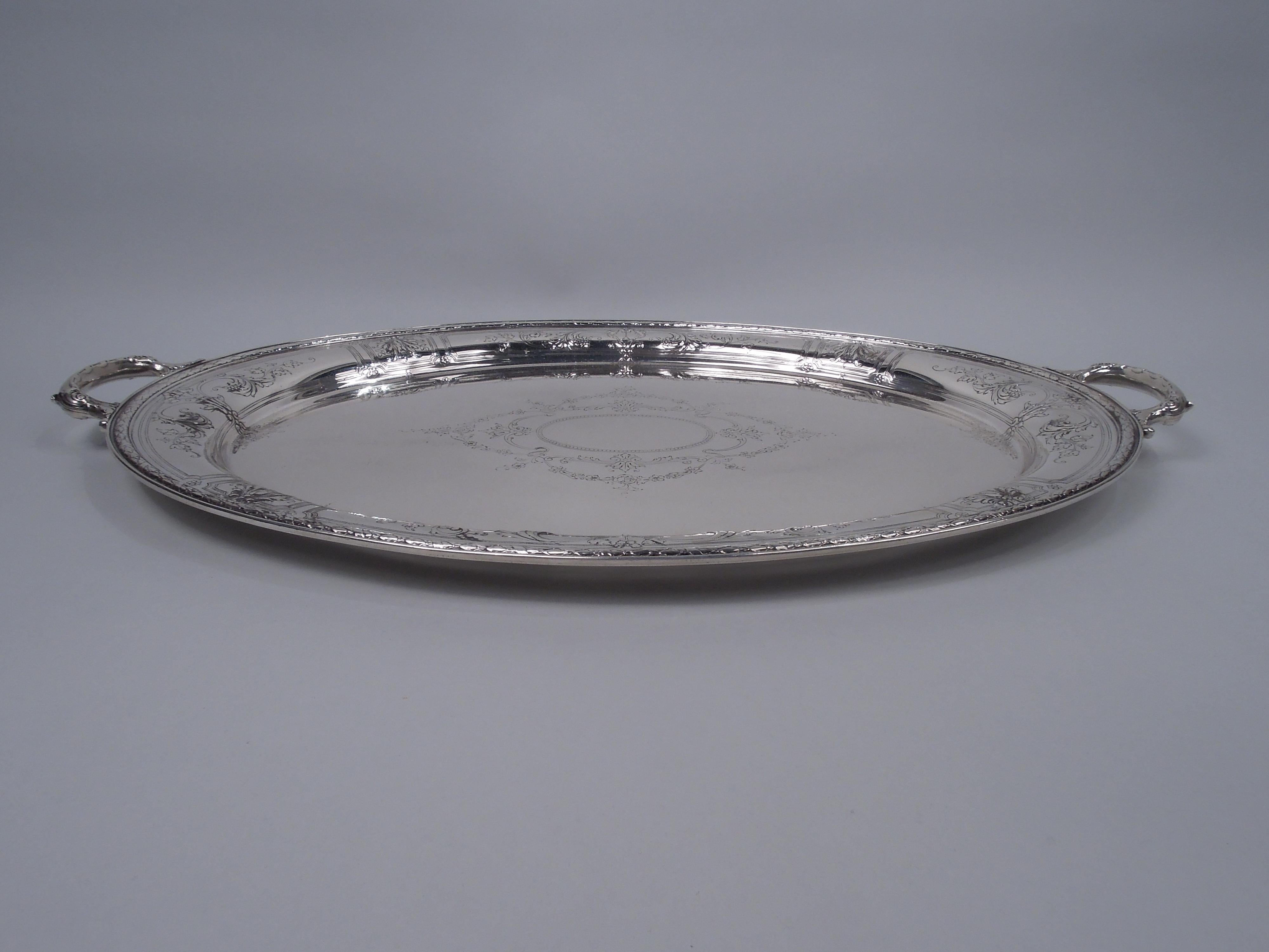 Maintenon sterling silver serving tray. Made by Gorham in Providence in 1923. Oval with leaf-capped and -mounted c-scroll side handles. Well has engraved beaded oval frame (vacant) in garland surround. Tapering shoulder with chased scrolls and