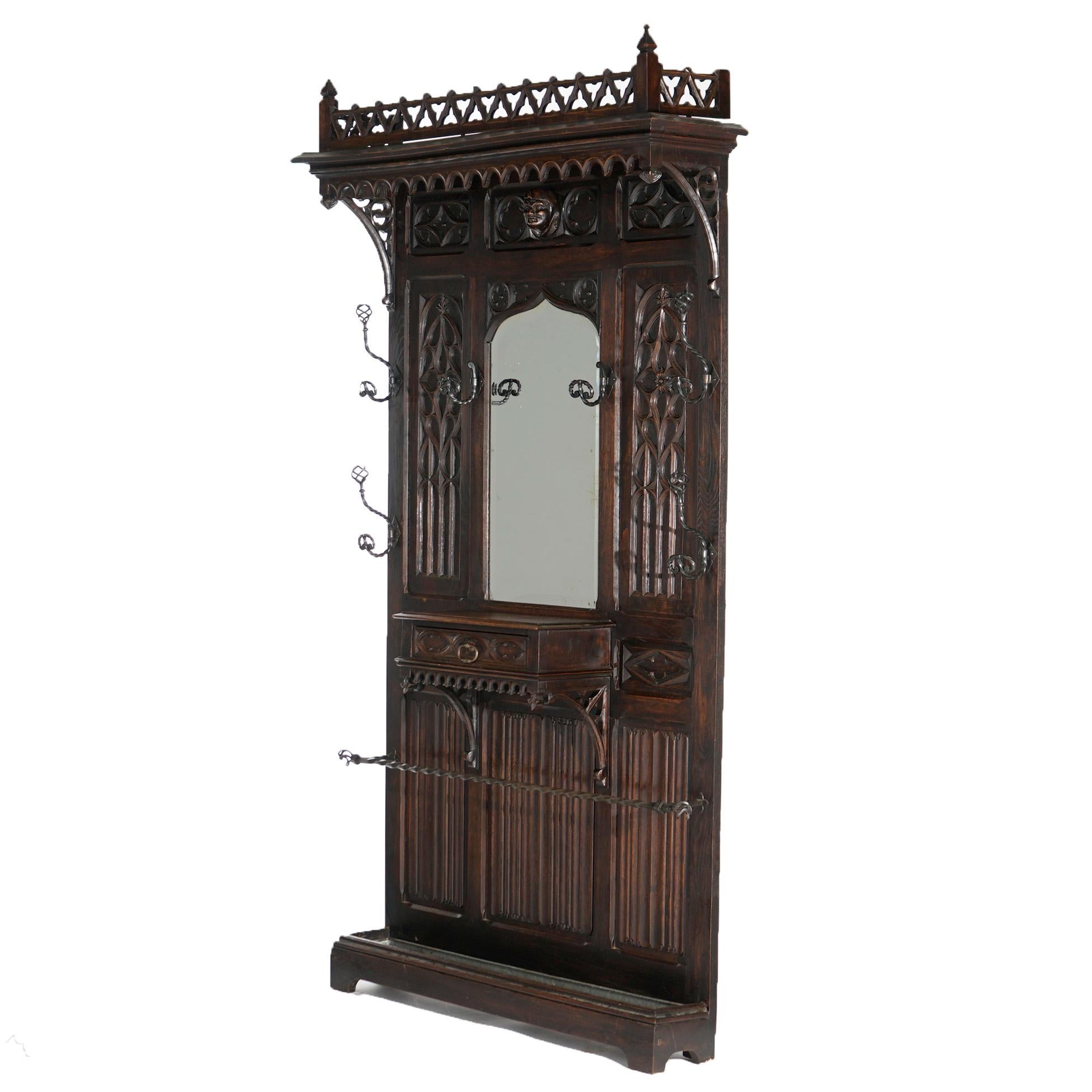 An oversized antique Gothic Revival figural hall mirror offers carved English oak construction with upper pierced gallery over frieze having central mask, arch form mirror, hardware for garments and central drawer, c1900

Measures- 93'' H x 50.5'' W