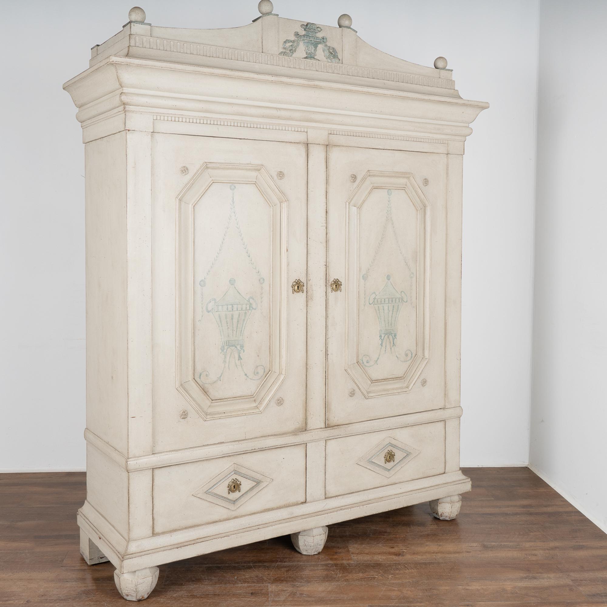 Statuesque gray armoire with beautiful paneled doors, impressive raised crown with large round finials and raised on large carved feet.
This elegant armoire was crafted in the mid 1800's and given a newer painted finish and adjustable shelving