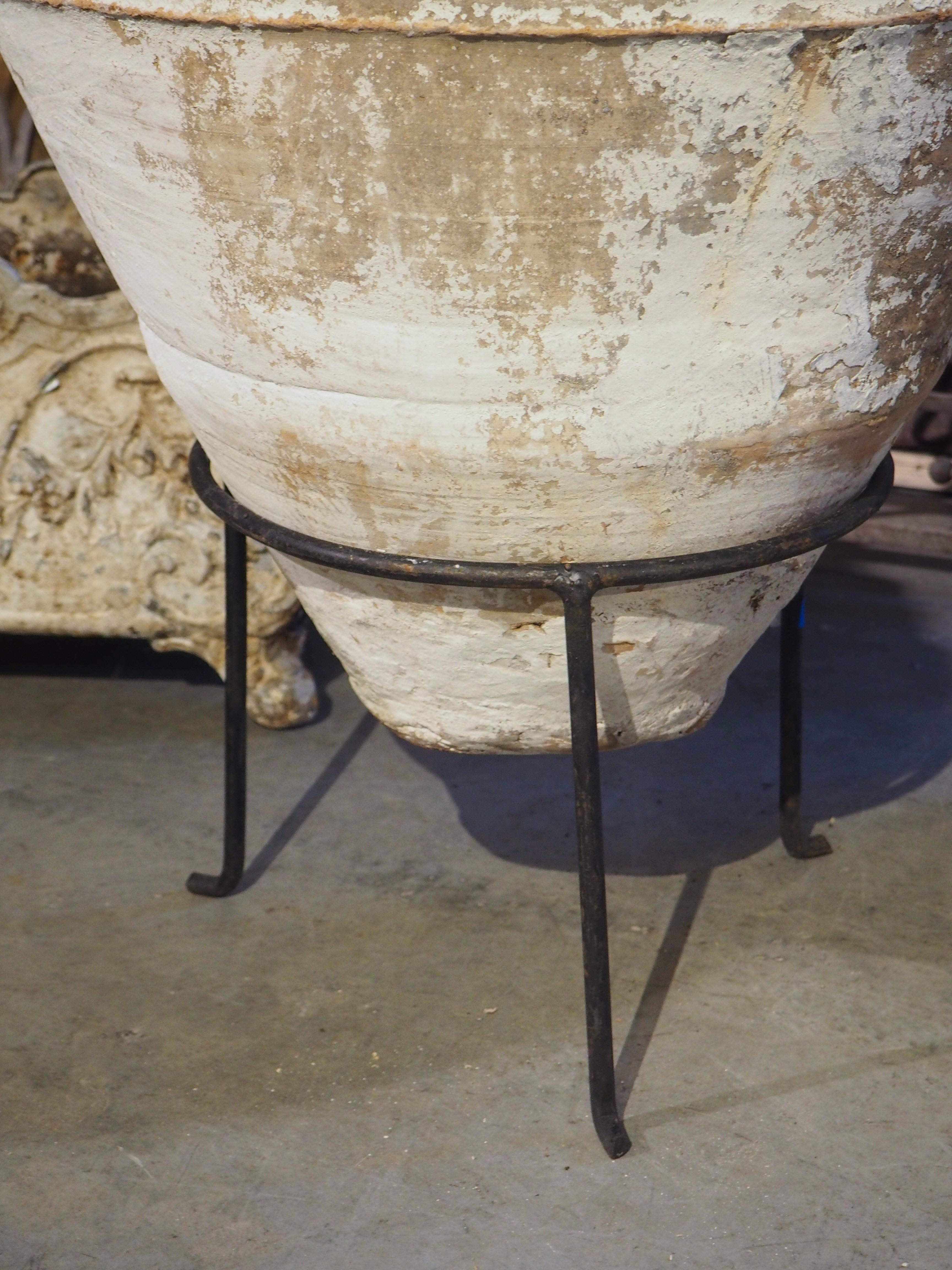 Known in Greece as a koroniotiko, this olive oil or grain pot dates to circa 1890. The large, hand-thrown terra cotta pot, which was painted white, sits in a painted black iron stand that was added more recently. Koroniotikos pots often have