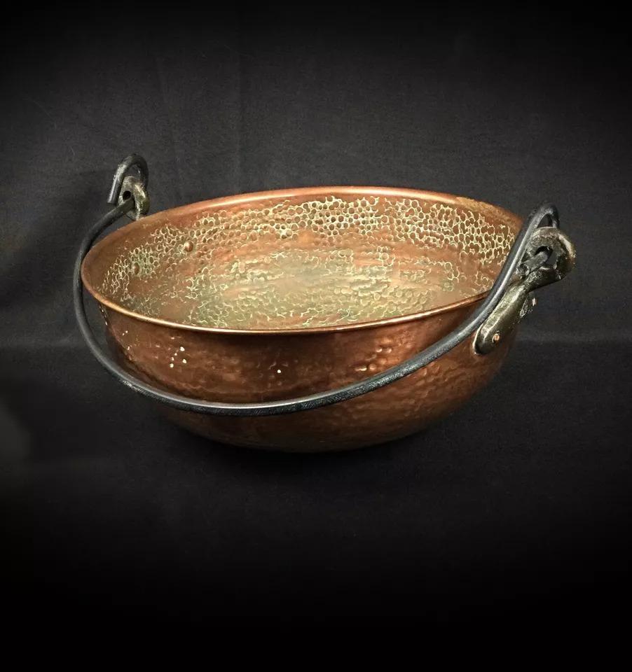 This large antique cauldron, crafted from hammered copper with a sturdy forged iron handle, is a timeless piece that reflects traditional craftsmanship. The cauldron is in good condition, with some oxidation marks that can be polished to restore its