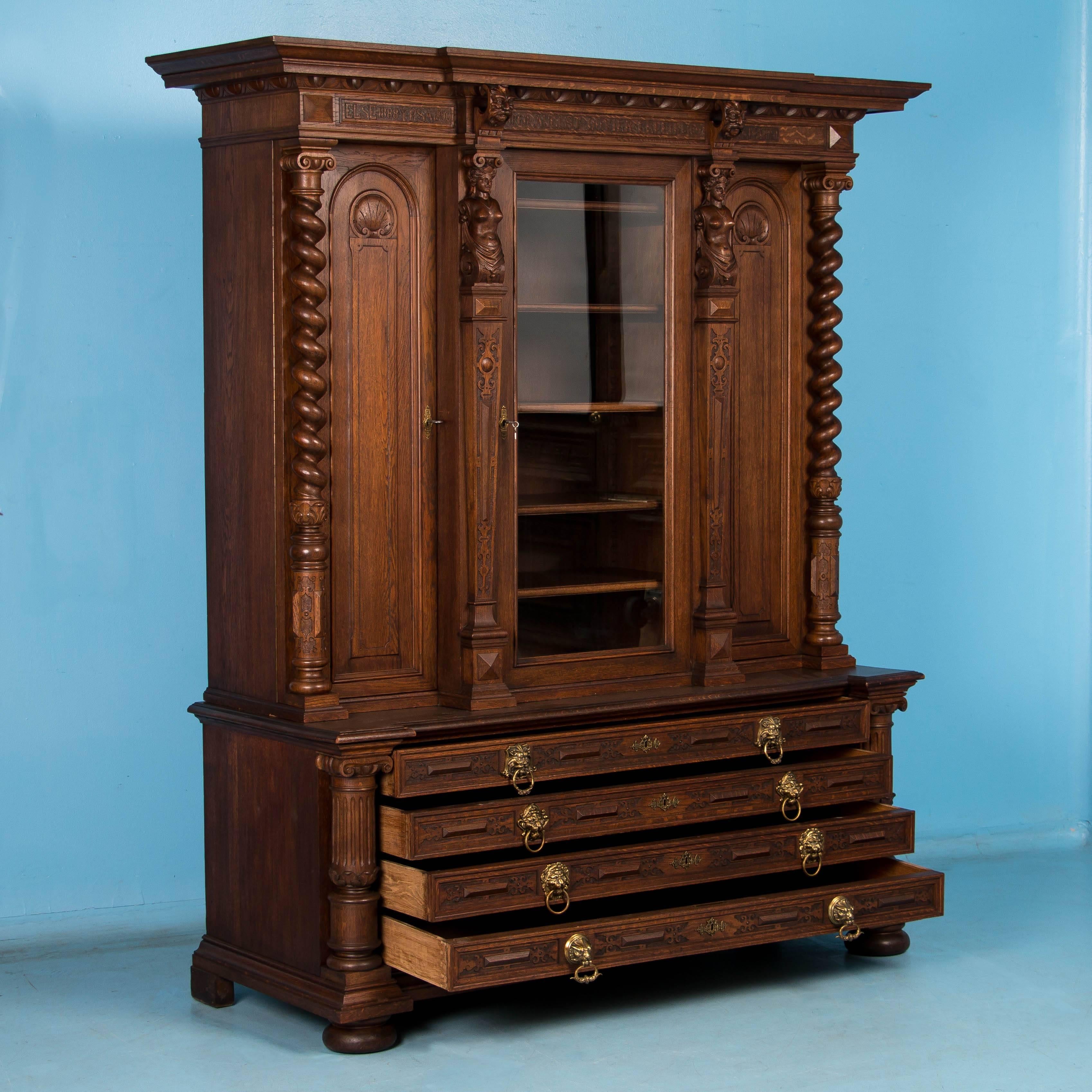 Impressive and statuesque, this extraordinary three door oak bookcase has hand carved columns and figureheads among its many elaborate features. The most notable carved elements are found in the crown where the family name Duvier is flanked by the